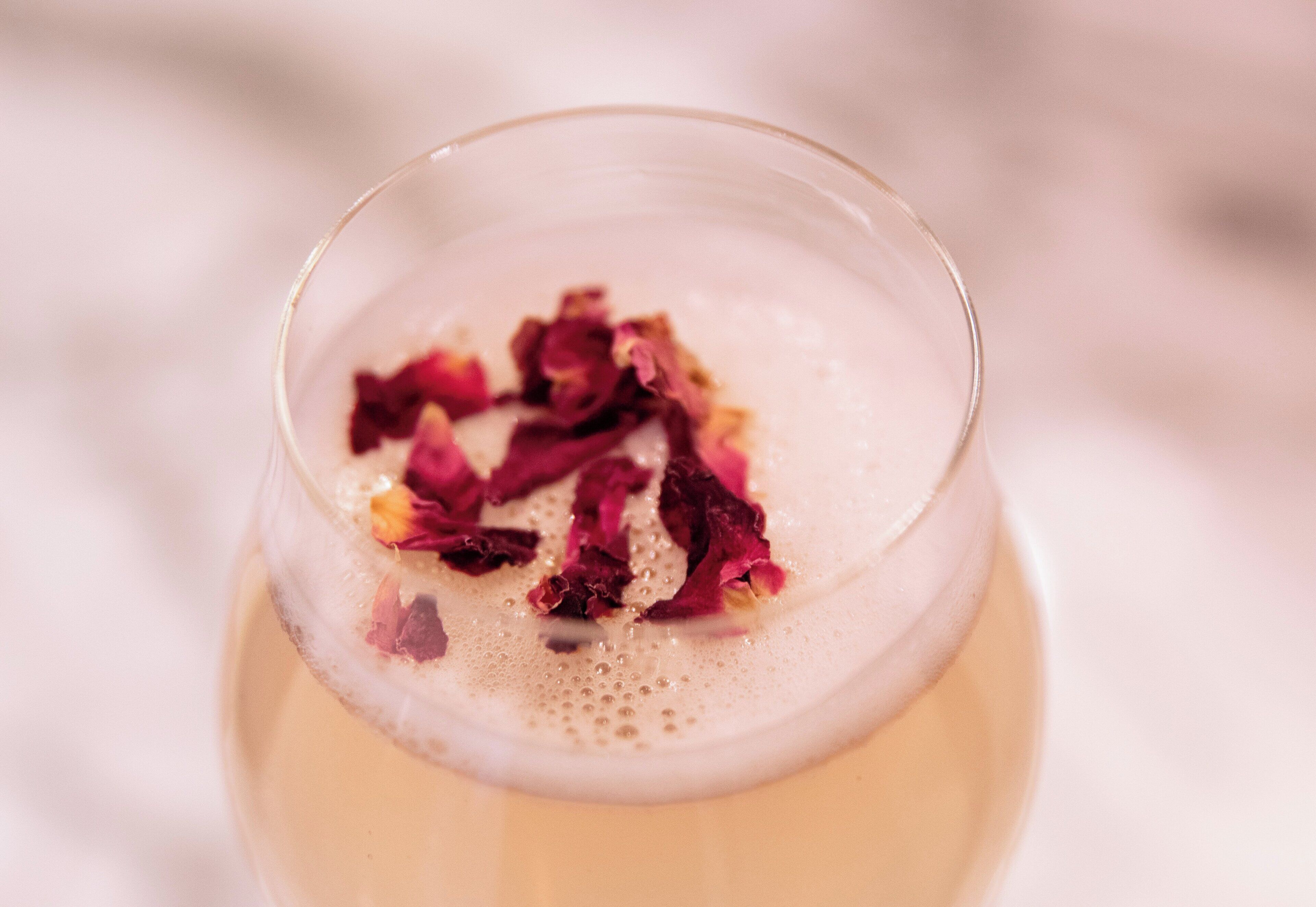 Un gros plan d’un verre contenant une boisson mousseuse et des pétales de rose.