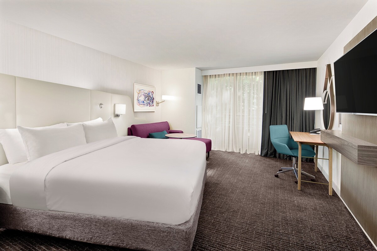 A hotel room with a large bed, a desk, a chair, and a TV.
