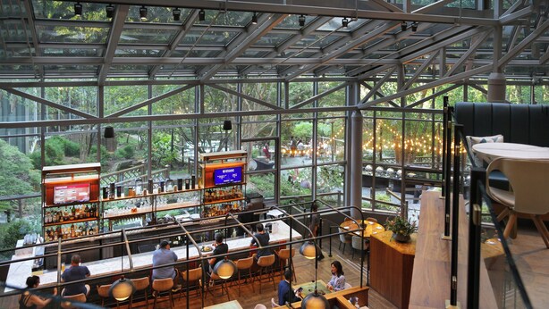 Eine moderne Bar mit hoher Decke und großen Fenstern mit Blick auf einen üppigen Garten.