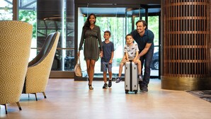 Eine Familie mit Kind und Koffer in einer modernen Lobby mit gemusterten Stühlen und einer großen Holzsäule.