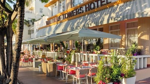 An outdoor seating area with tables and chairs, potted plants, and a building with a sign reading "Waldorf Towers Hotel". - Waldorf Towers South Beach (Miami Beach)