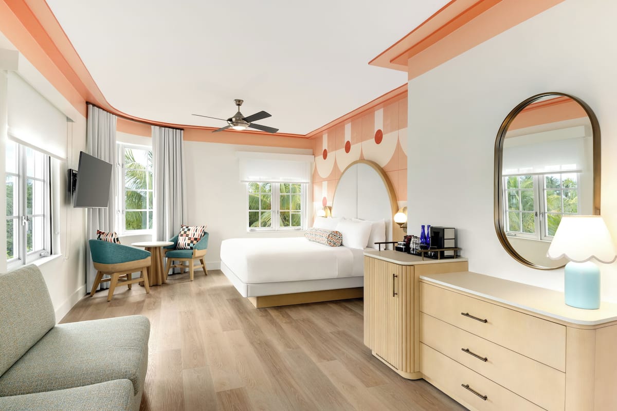Hotelkamer met een bed, een bureau, een stoel, een televisie, een plafondventilator en een grote spiegel.