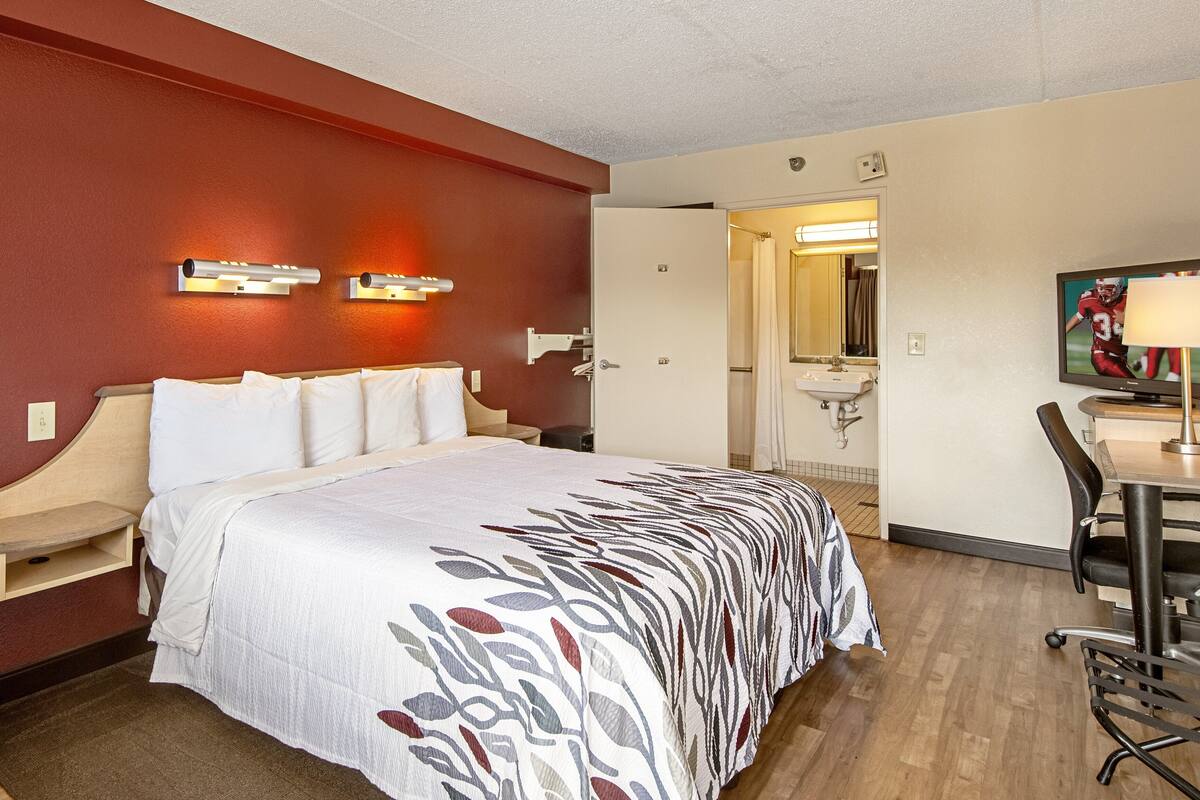 Ein Hotelzimmer mit einem großen Bett, einem Schreibtisch mit Stuhl, einem Fernseher und einem durchgegangenen Tür sichtbaren Badezimmer.