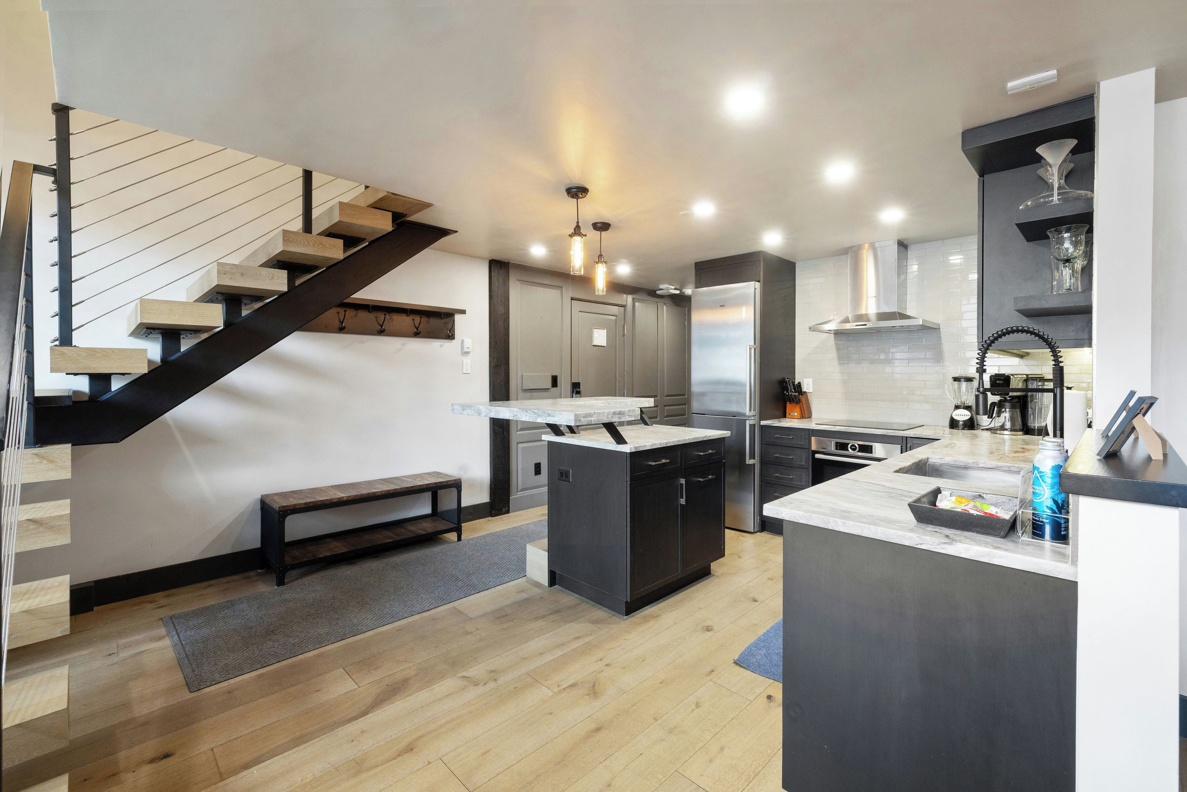 A modern kitchen with a central island, built-in appliances, and a wooden staircase.