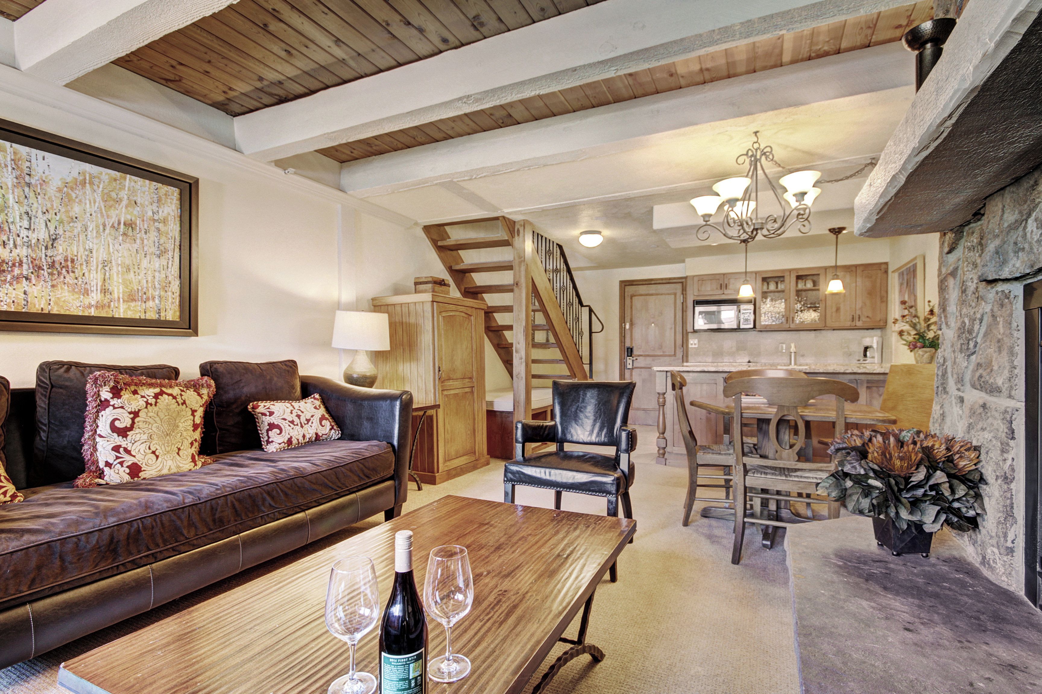 A spacious living area with a wooden dining table, leather sofa, and a staircase leading to a kitchen.