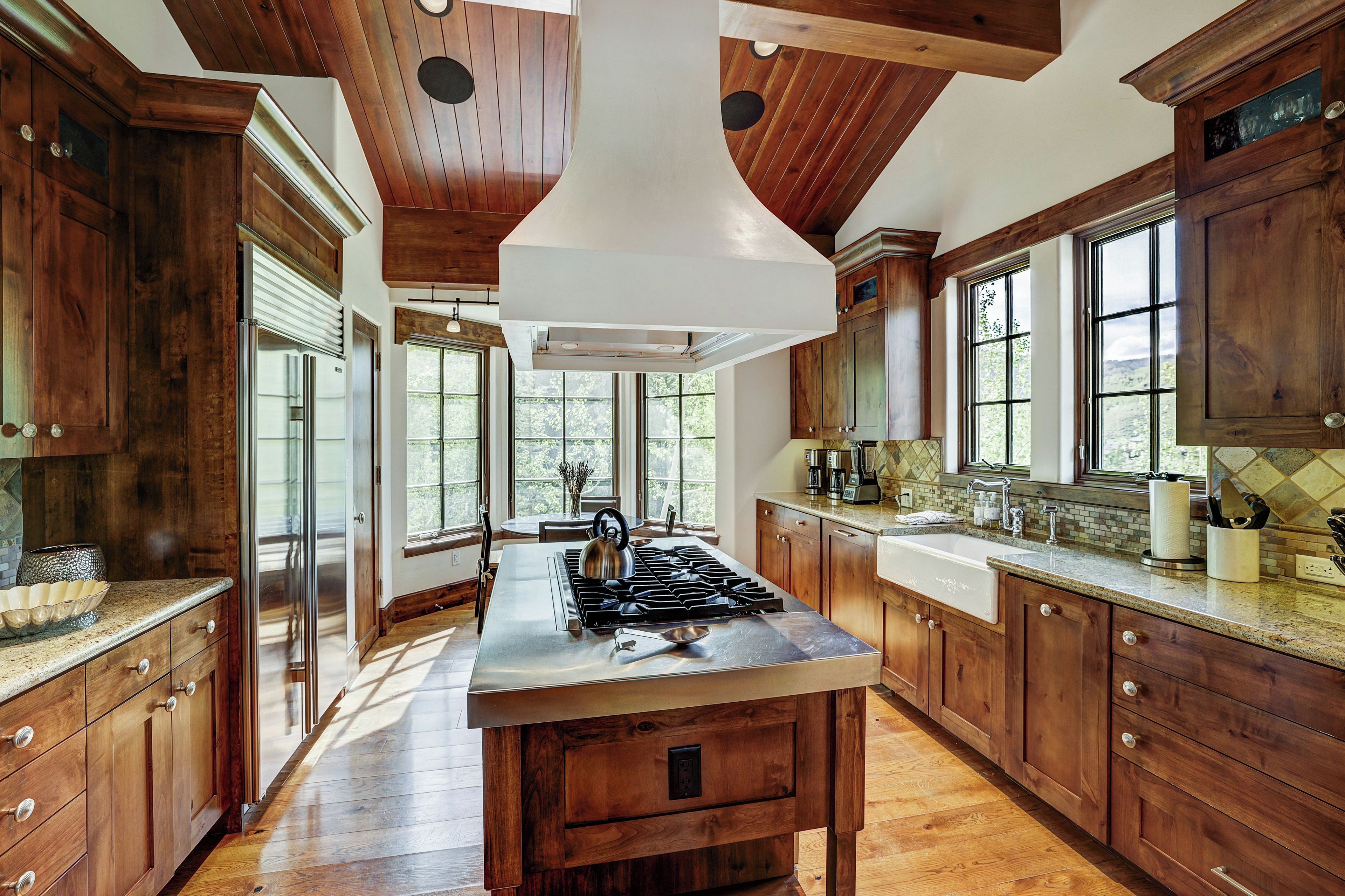 A spacious kitchen with wooden cabinets, a central island, stainless steel appliances, and large windows allowing natural light.