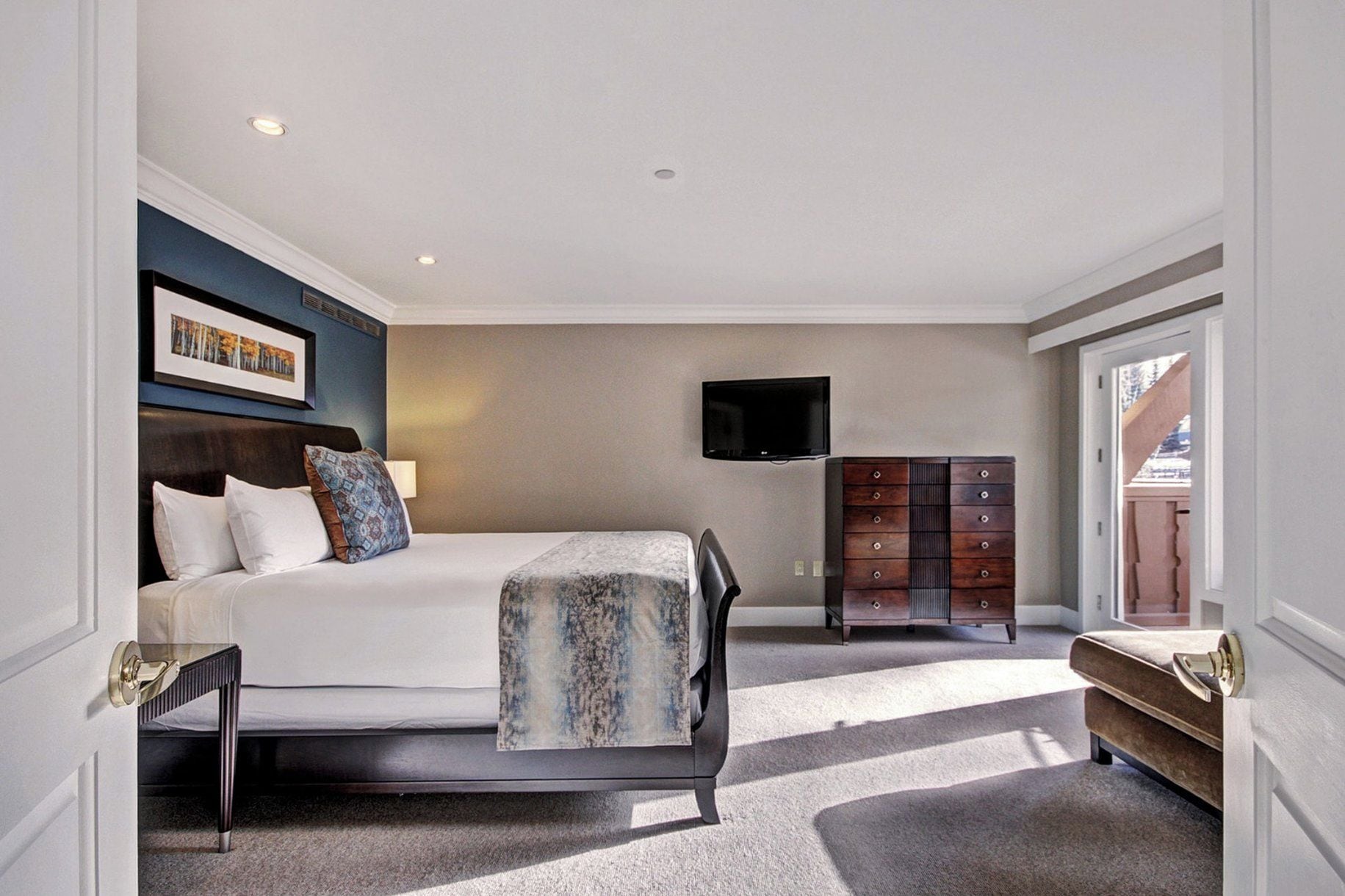 Een moderne hotelkamer met een bed, een dressoir, een televisie en uitzicht op het groen.