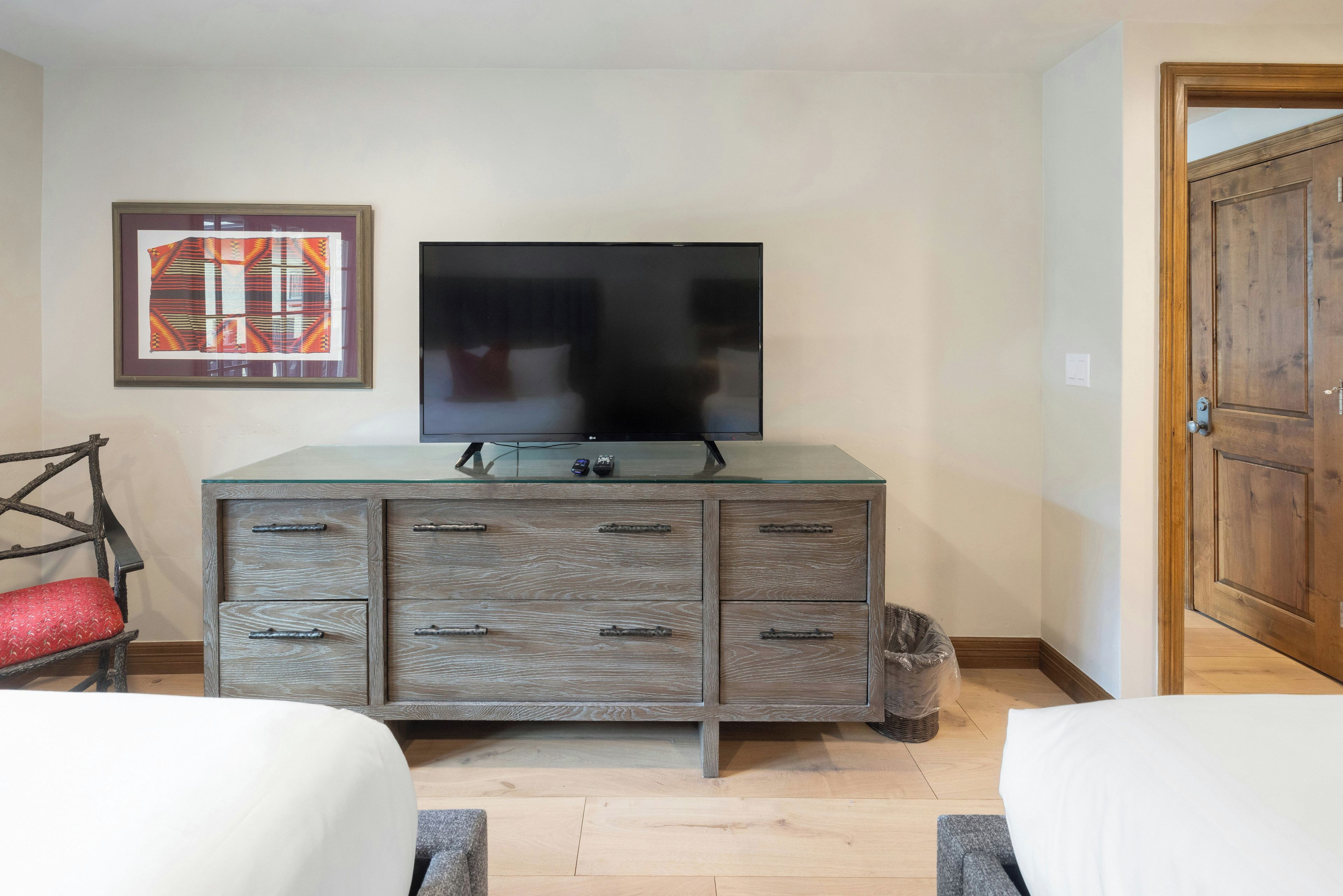 A room with a bed, a dresser with a TV, a framed picture, and a wooden door.