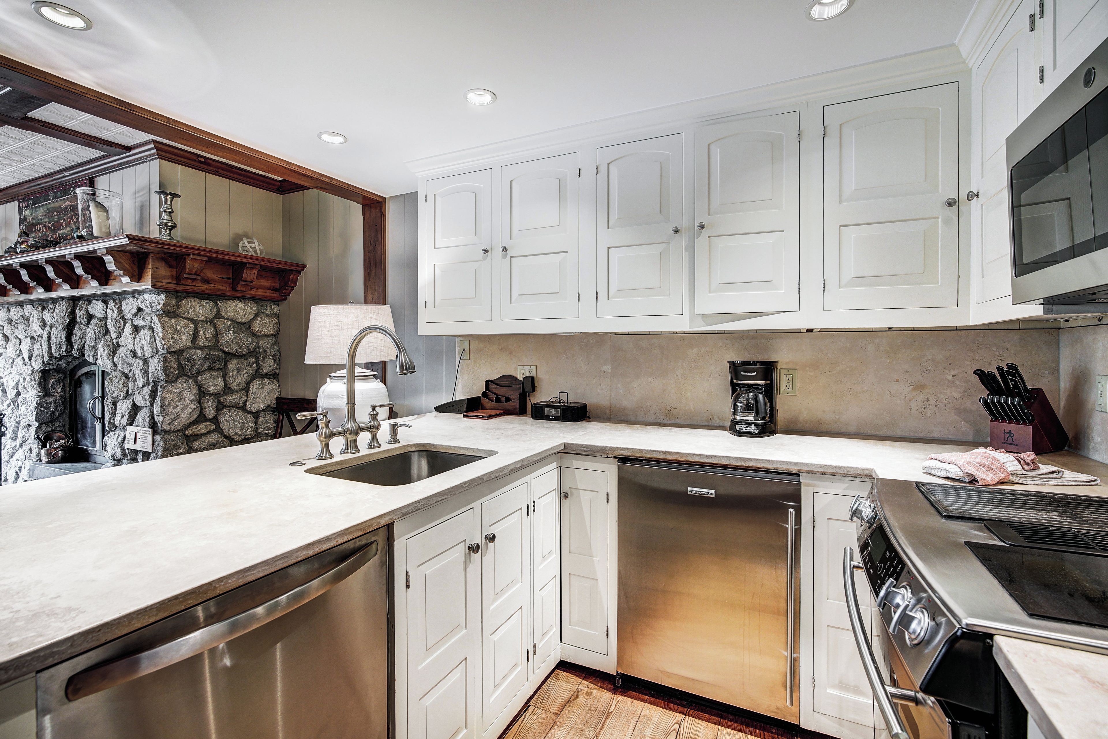 A modern kitchen with white cabinets, a built-in dishwasher, a stove, and a stone accent wall.