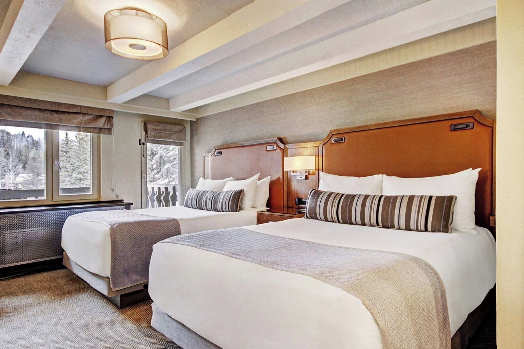 Habitación de hotel con dos camas, un ventanal grande y vistas a árboles.