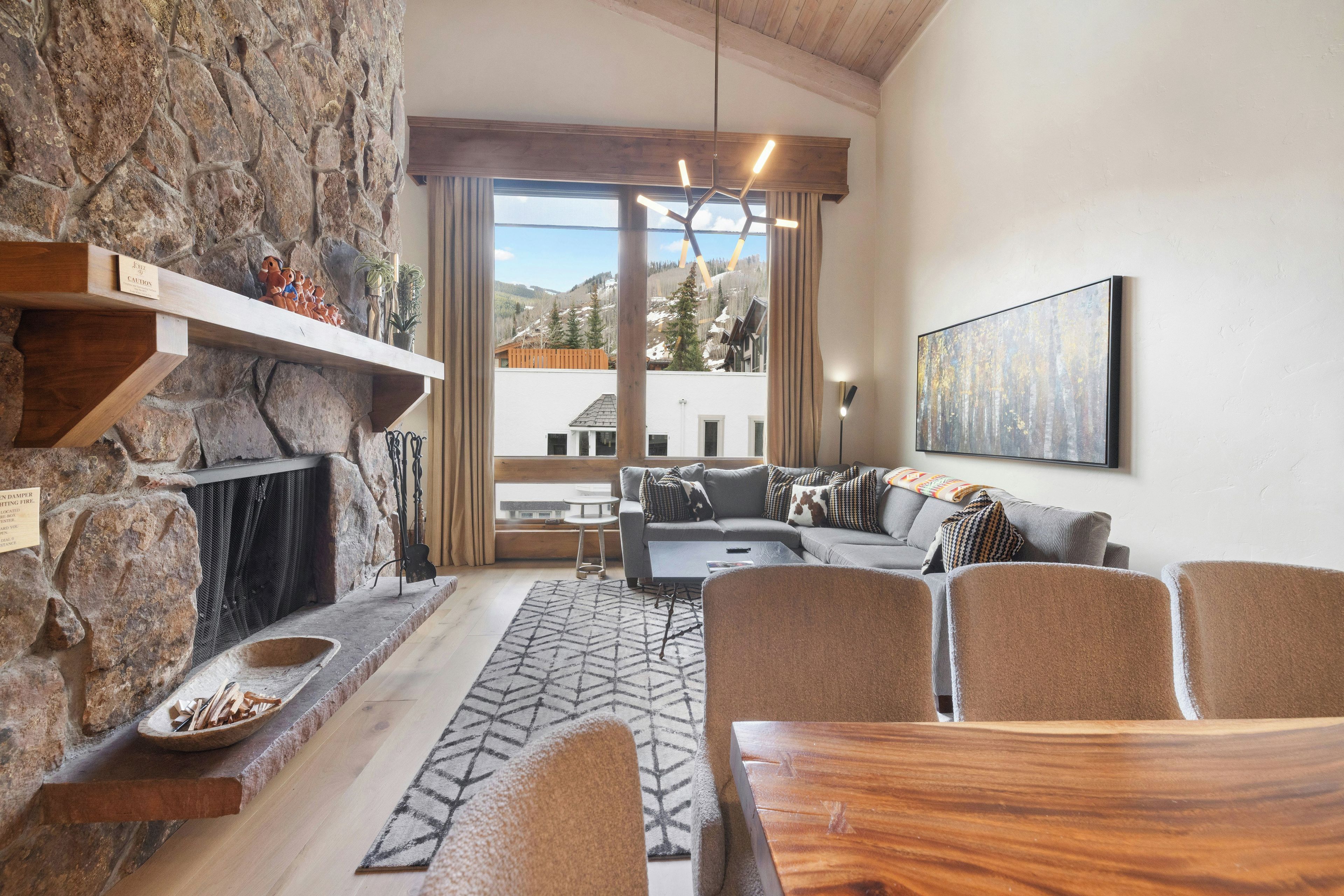 Una chimenea de piedra, una mesa de comedor de madera, un conjunto de sofá y un ventanal con vistas a la montaña.