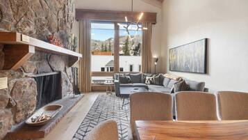 Una chimenea de piedra, una mesa de comedor de madera, un conjunto de sofá y un ventanal con vistas a la montaña.