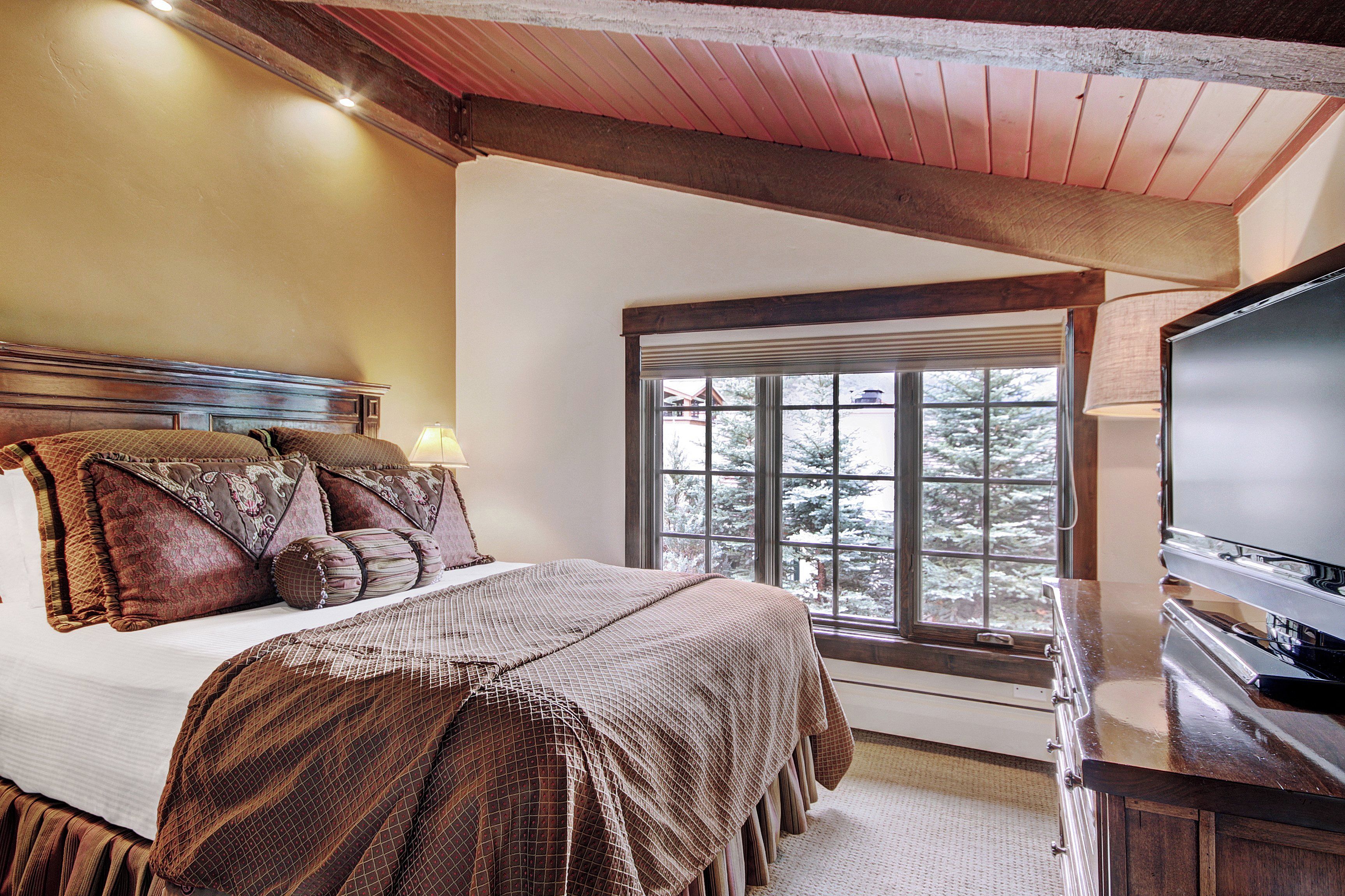 A bedroom with a large bed, a television, and a window with a view of trees.