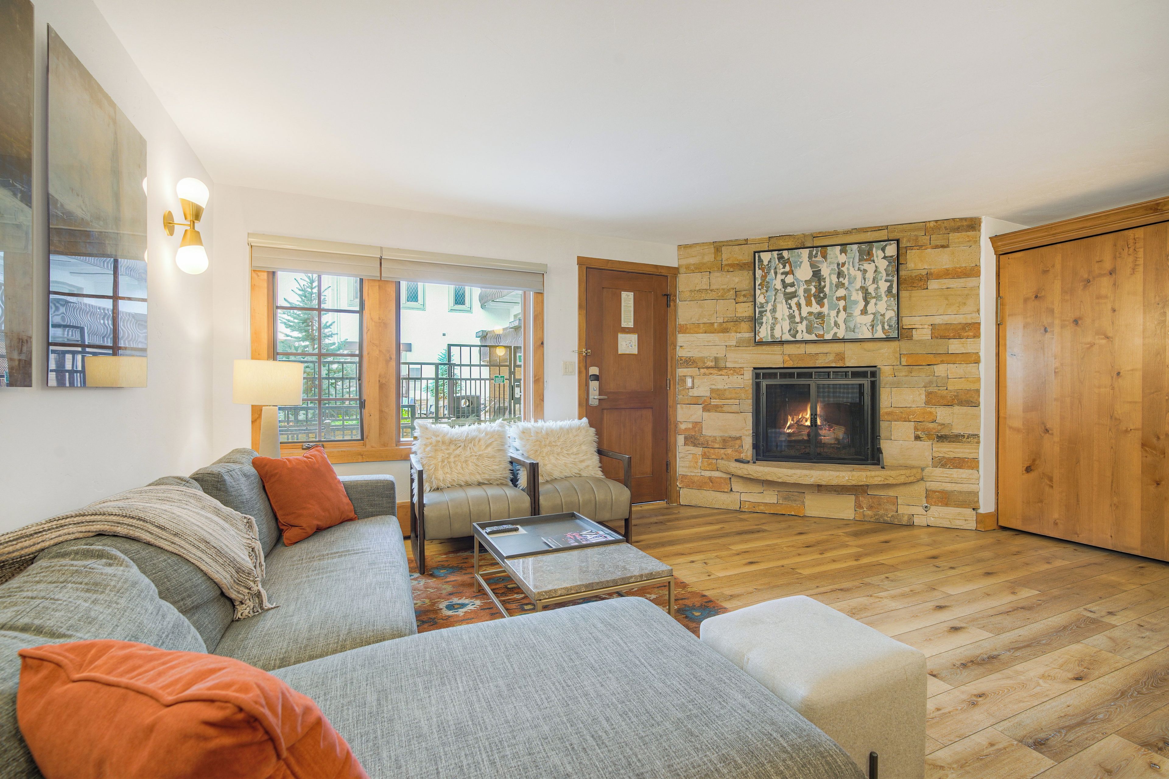 A cozy living room with a stone fireplace, a sofa, a coffee table, and a view through a glass door.