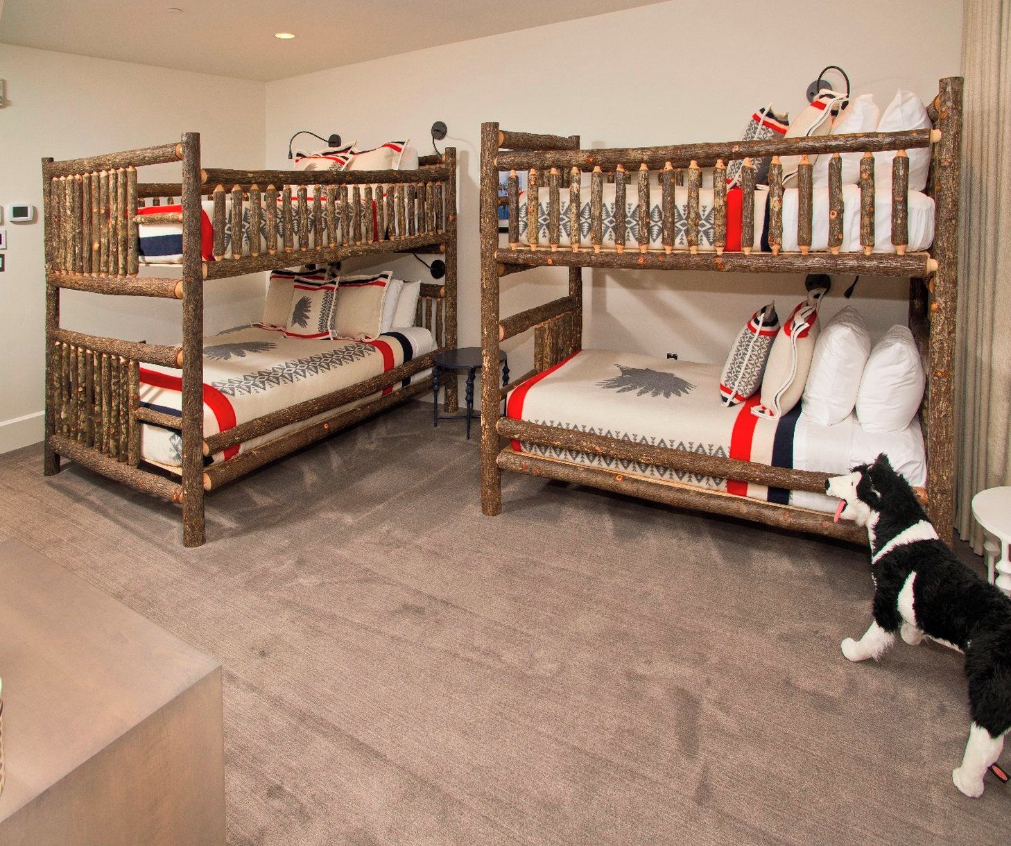 Two bunk beds with wooden frames and patterned bedding, a small table, and a cat in a room with carpeted flooring.