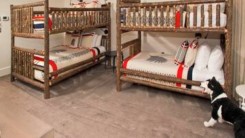 Two bunk beds with wooden frames and patterned bedding, a small table, and a cat in a room with carpeted flooring.