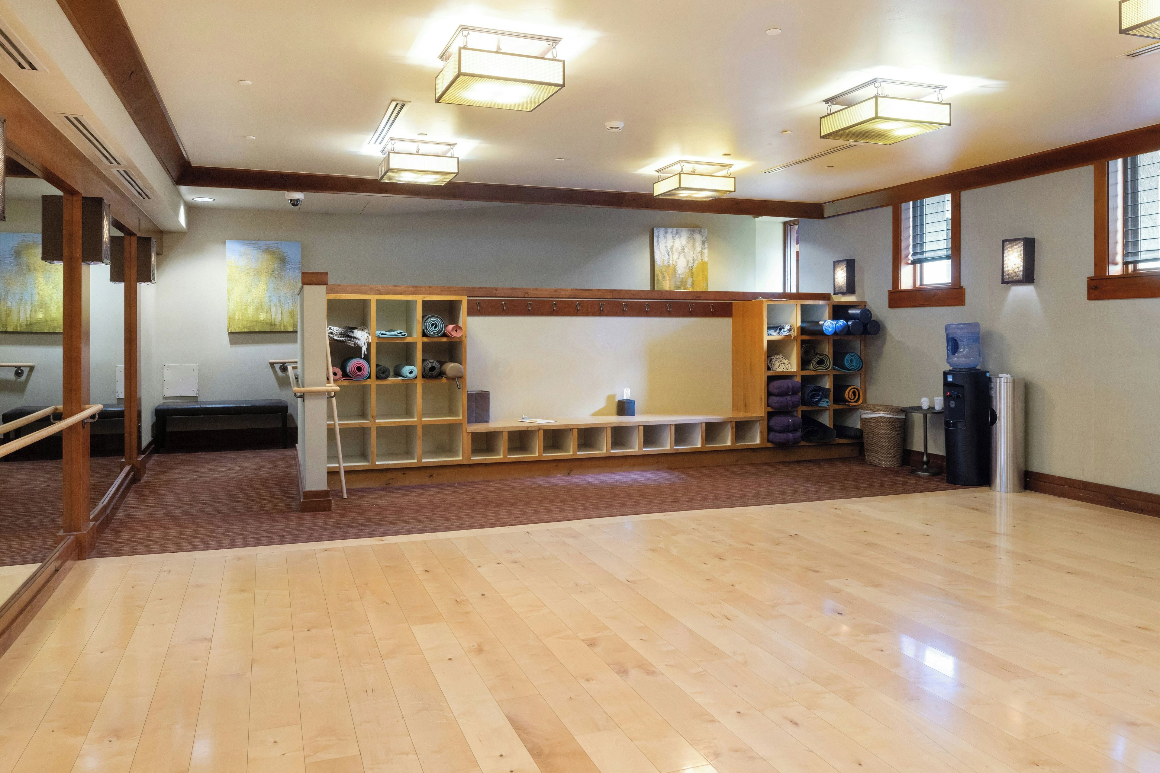 A spacious room with wooden flooring, a bench, and a wall-mounted rack with exercise equipment.