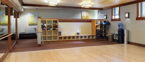 A spacious room with wooden flooring, a bench, and a wall-mounted rack with exercise equipment.