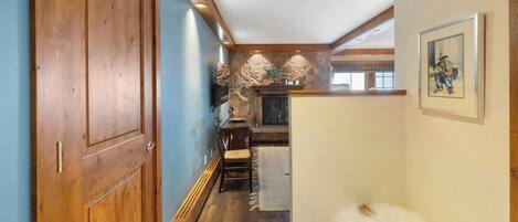 A hallway with wooden doors, a stone wall, a fireplace, and a framed picture on the wall.