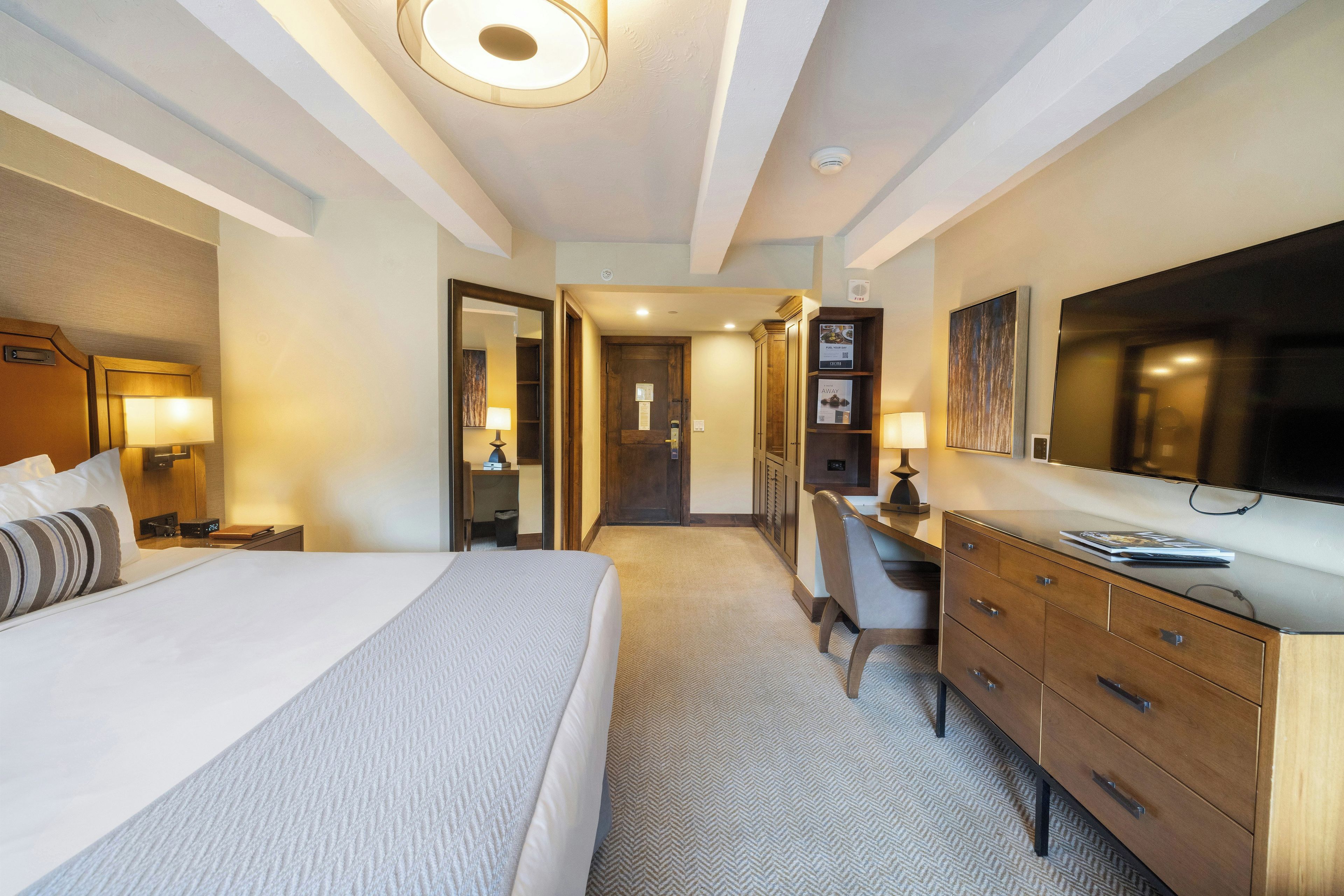 Habitación de hotel con cama, escritorio, cómoda y un espejo grande.