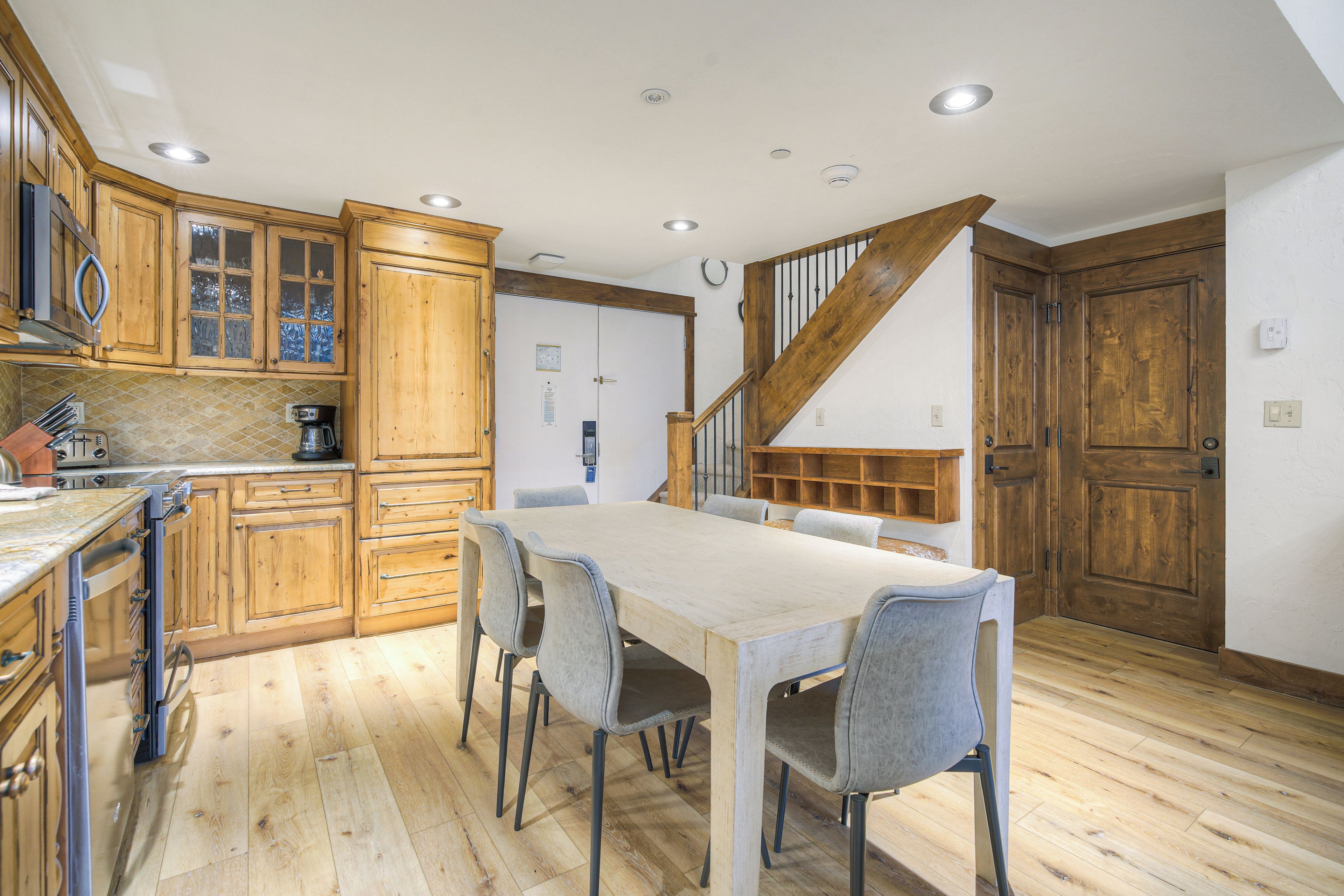 A kitchen with wooden cabinets, a dining table with chairs, and a staircase.