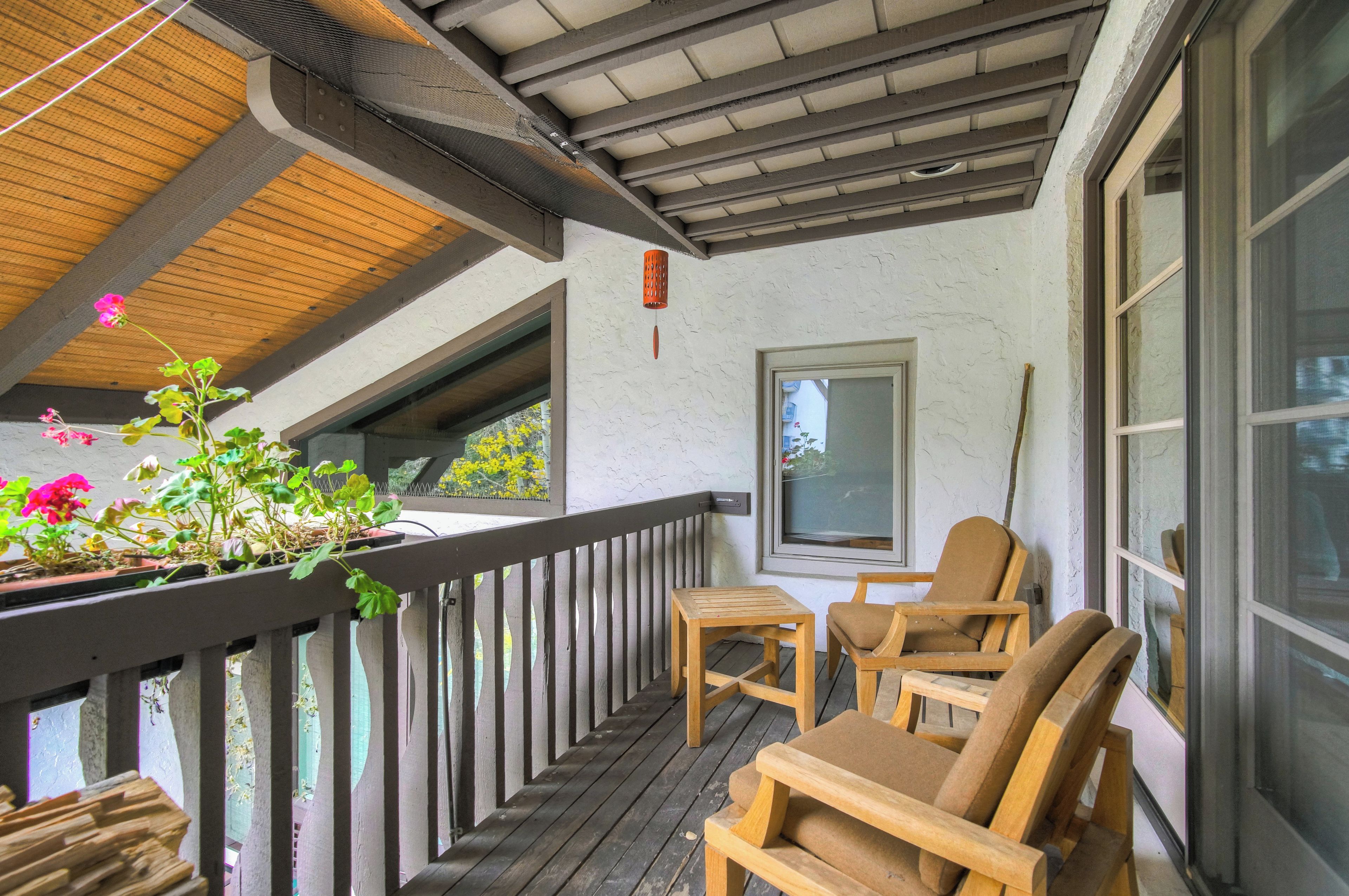 Une terrasse en bois avec une rambarde, deux chaises en bois, une petite table et des plantes en pot.