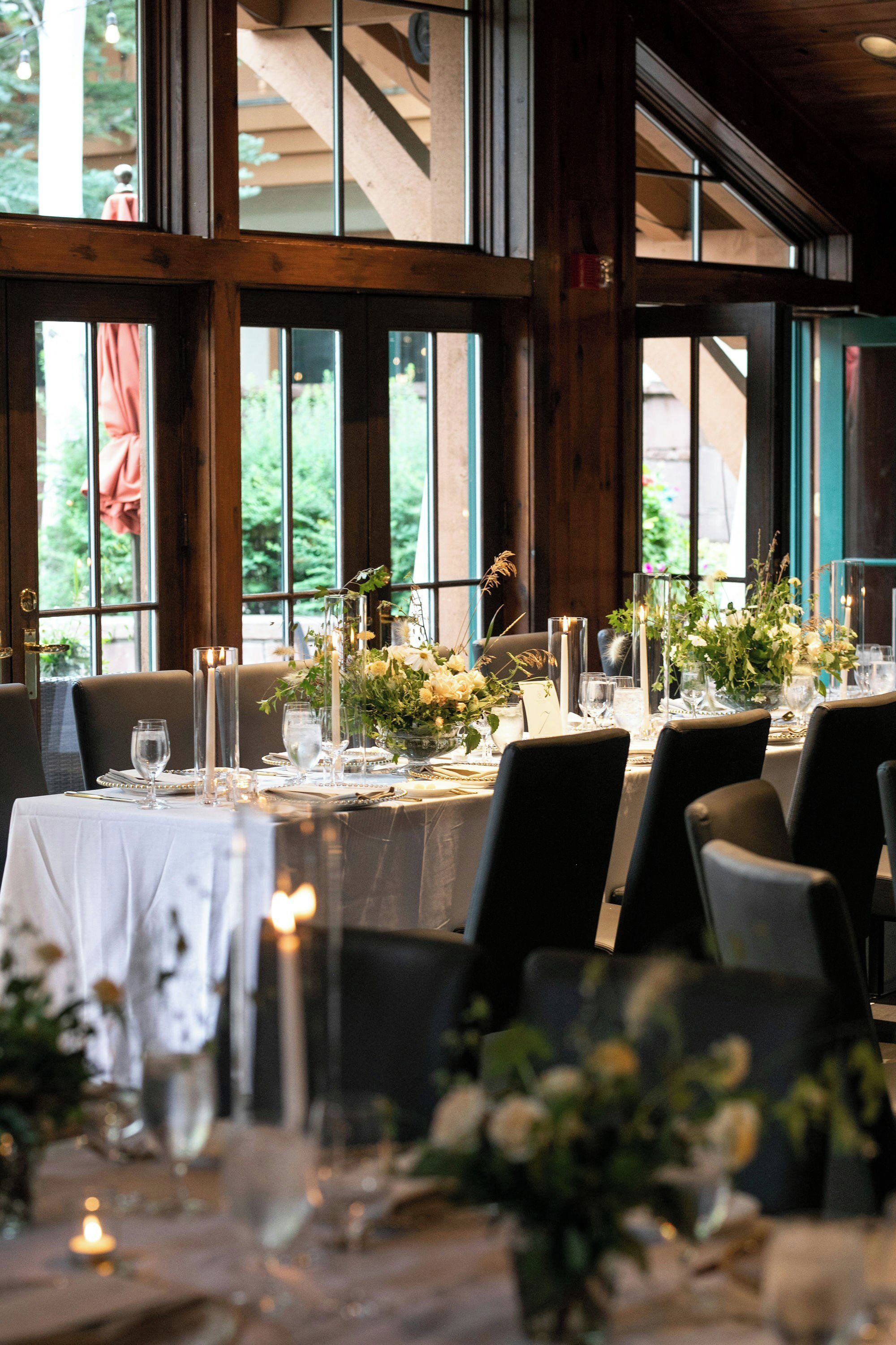 Un espace repas avec des tables dressées pour le dîner, agrémenté de bougies, de verres et de compositions florales.