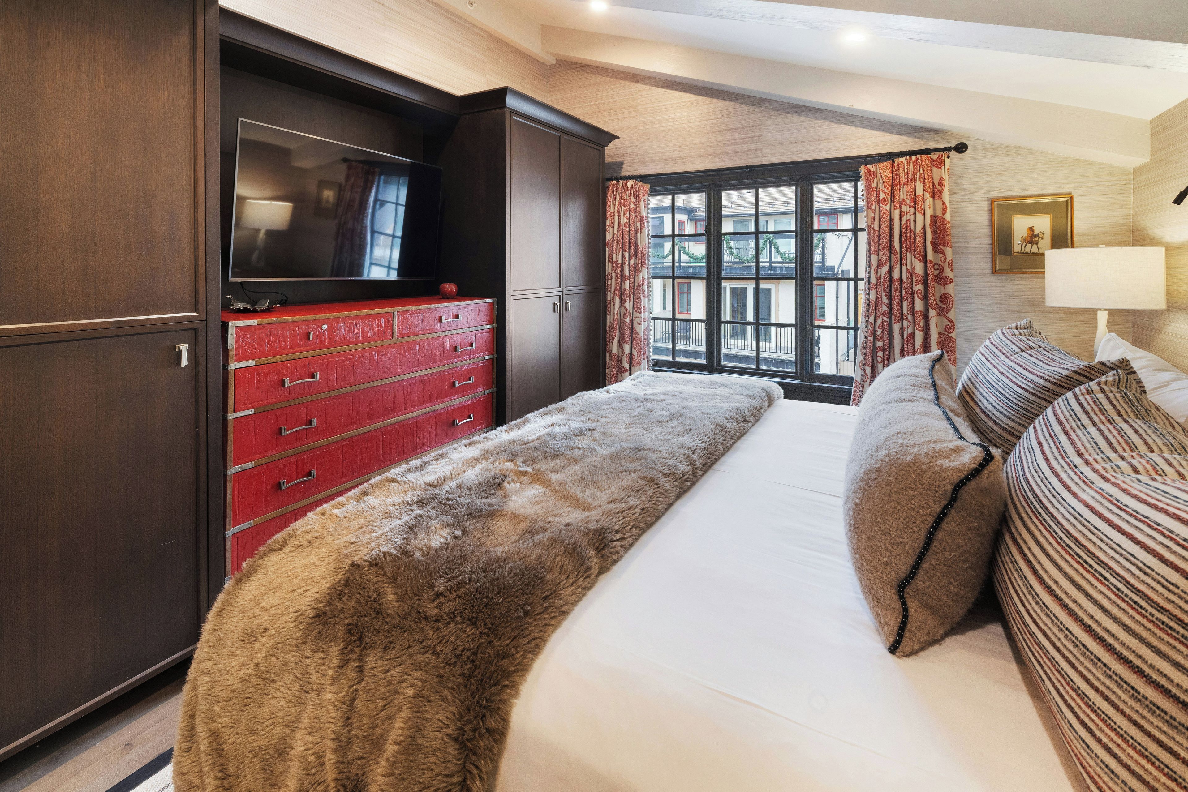 A bedroom with a large bed, a TV, a red dresser, and a window with curtains.