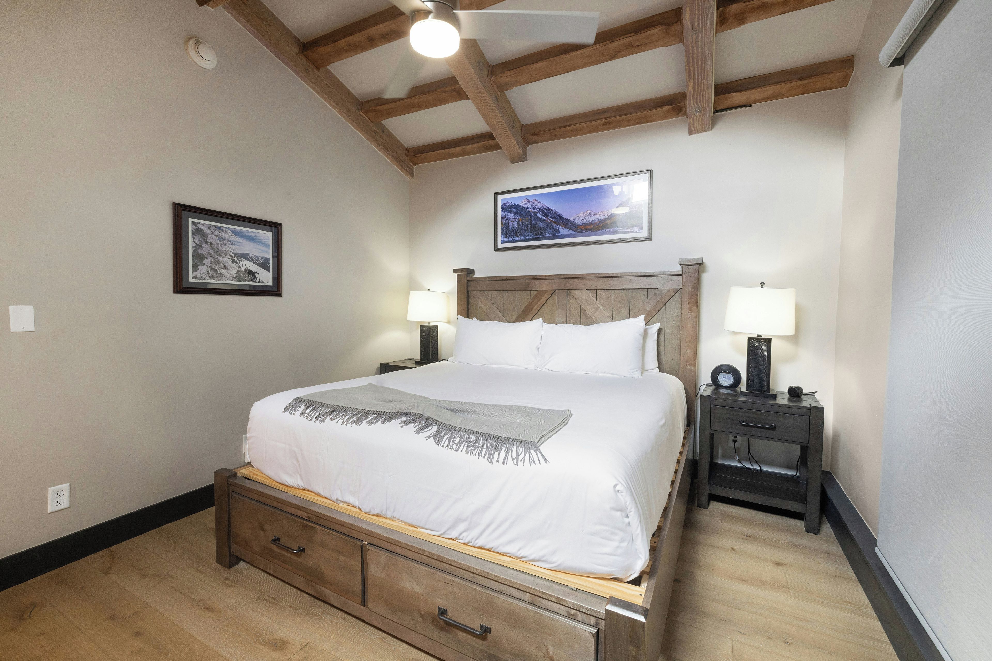 Une chambre à coucher avec un lit en bois, deux tables de chevet avec des lampes, un ventilateur de plafond et un tableau encadré au mur.