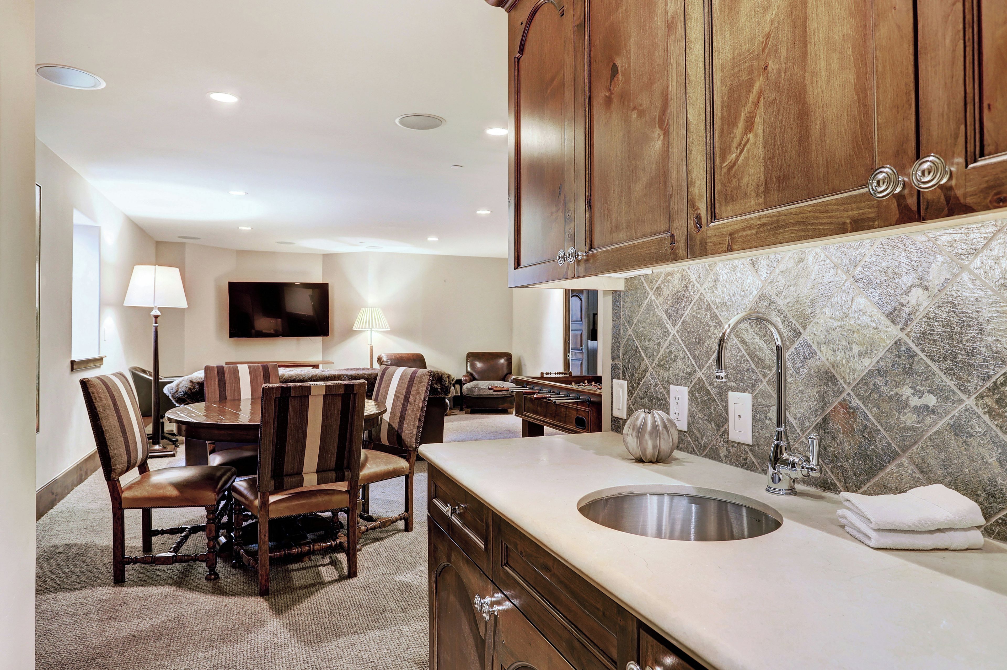 A modern kitchen with wooden cabinets, a large island with a sink, and a dining area with striped chairs.