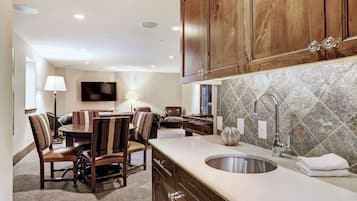 A modern kitchen with wooden cabinets, a large island with a sink, and a dining area with striped chairs.
