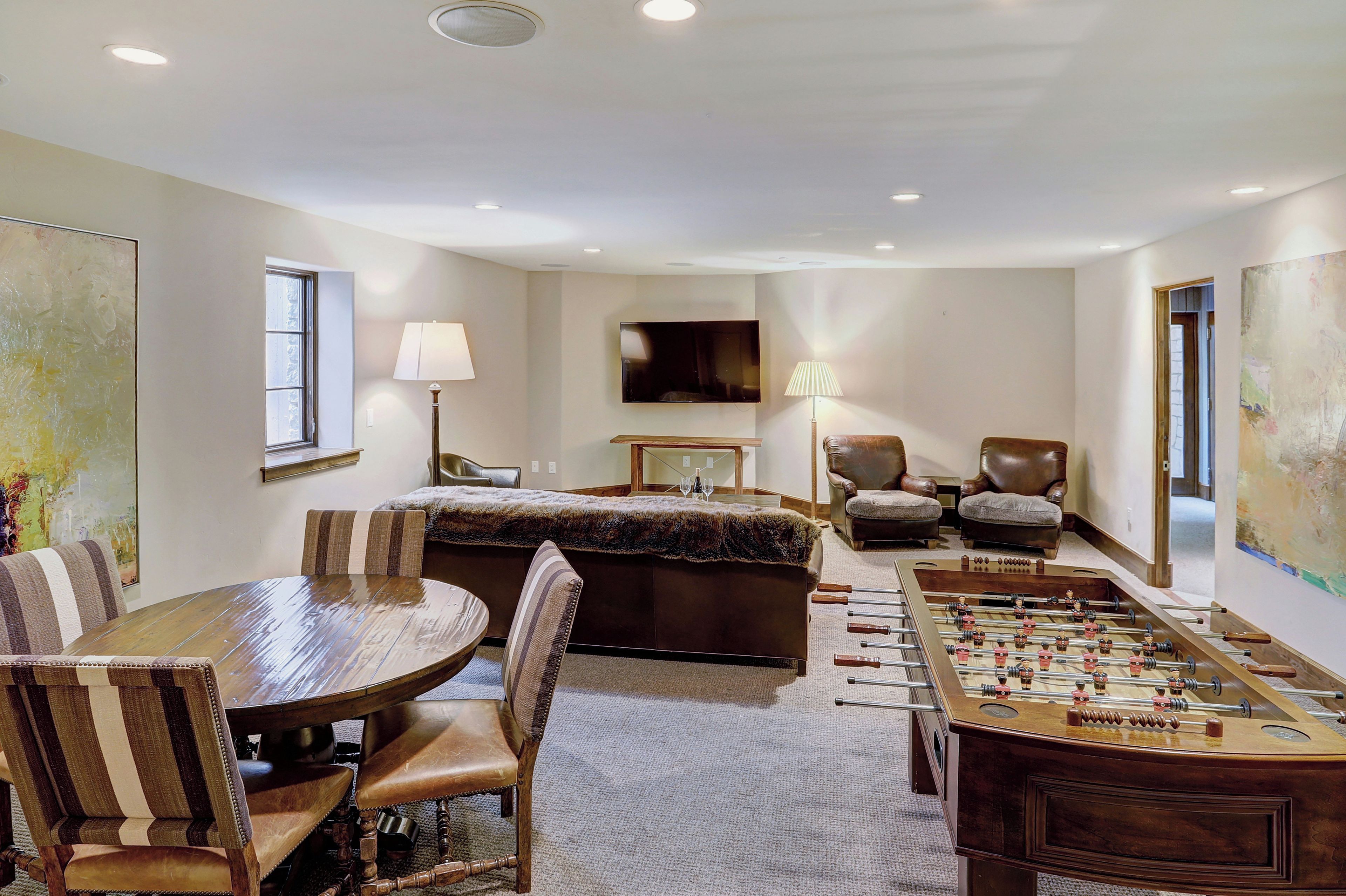 A room with a round table, chairs, a sofa, a TV, and an foosball table.