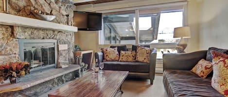 A living room with a stone fireplace, leather sofa, and a flat-screen TV mounted on the wall.
