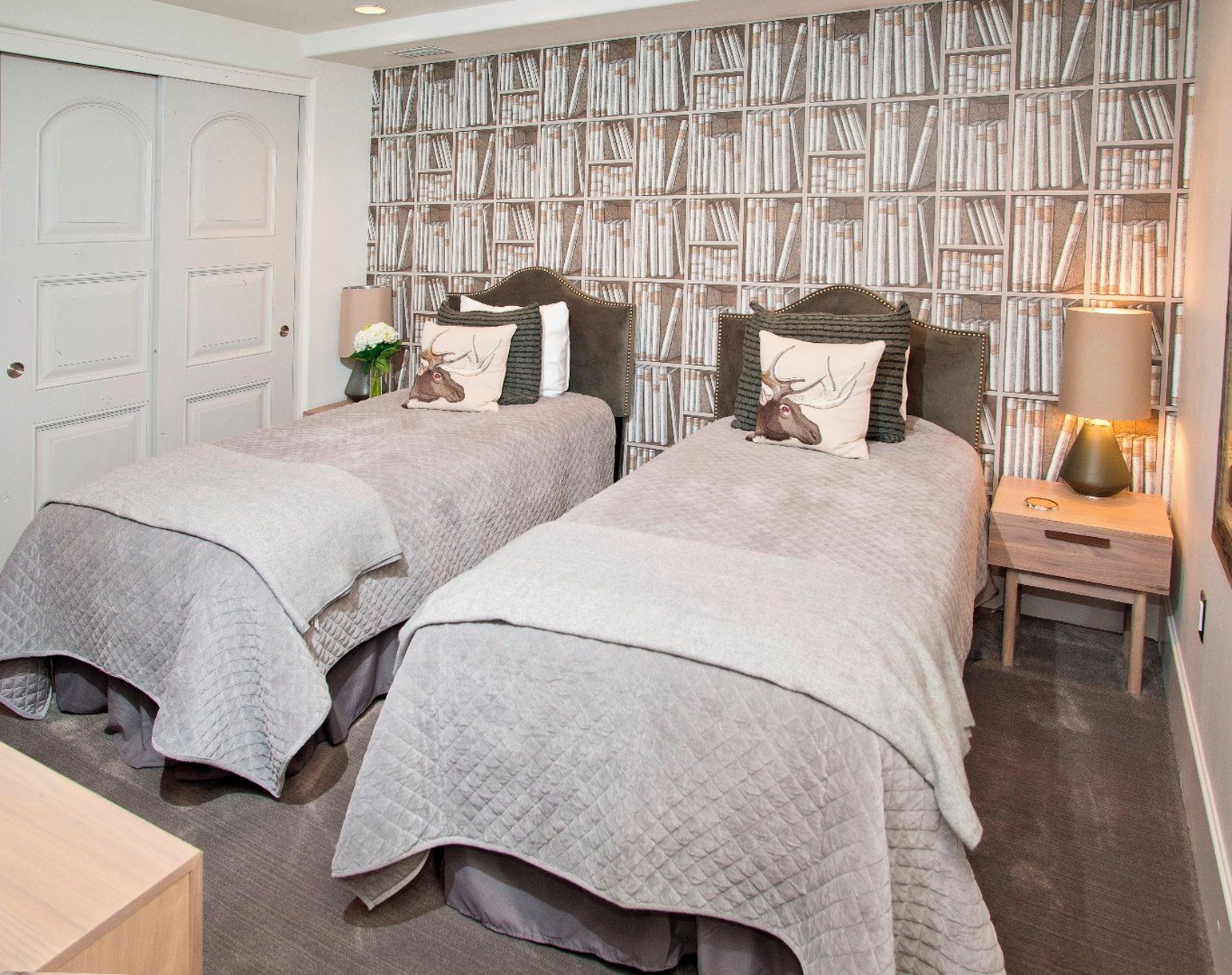 A bedroom with two beds, a bookshelf, a nightstand, and a door.