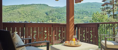 Un balcon doté de meubles en osier, d’une balustrade en bois et offrant une vue sur des collines verdoyantes.