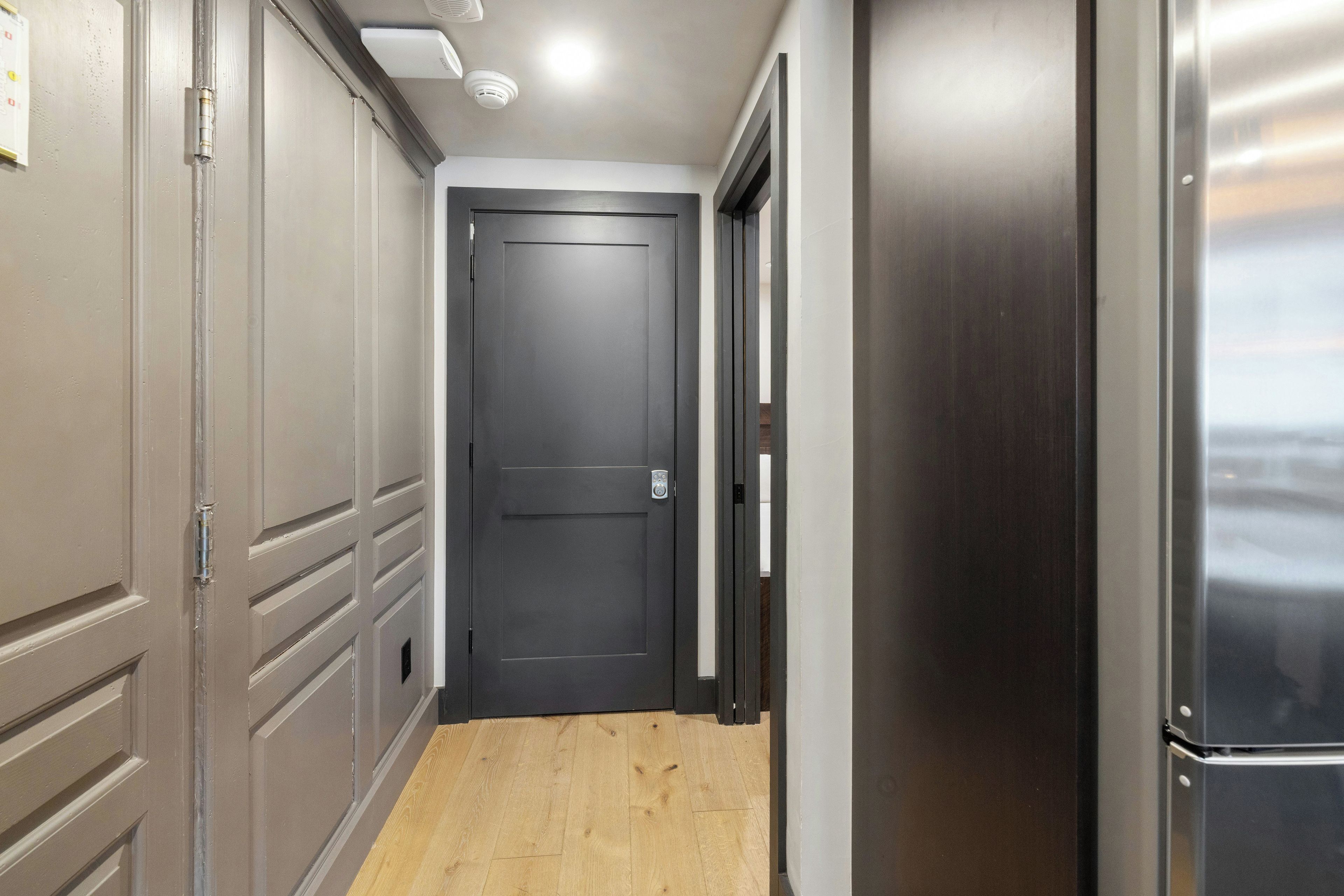 A hallway with a closed door, a refrigerator, and a wooden floor.