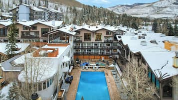 A resort with multiple buildings, a central swimming pool, and a mountainous backdrop.