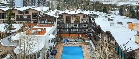 A resort with multiple buildings, a central swimming pool, and a mountainous backdrop.