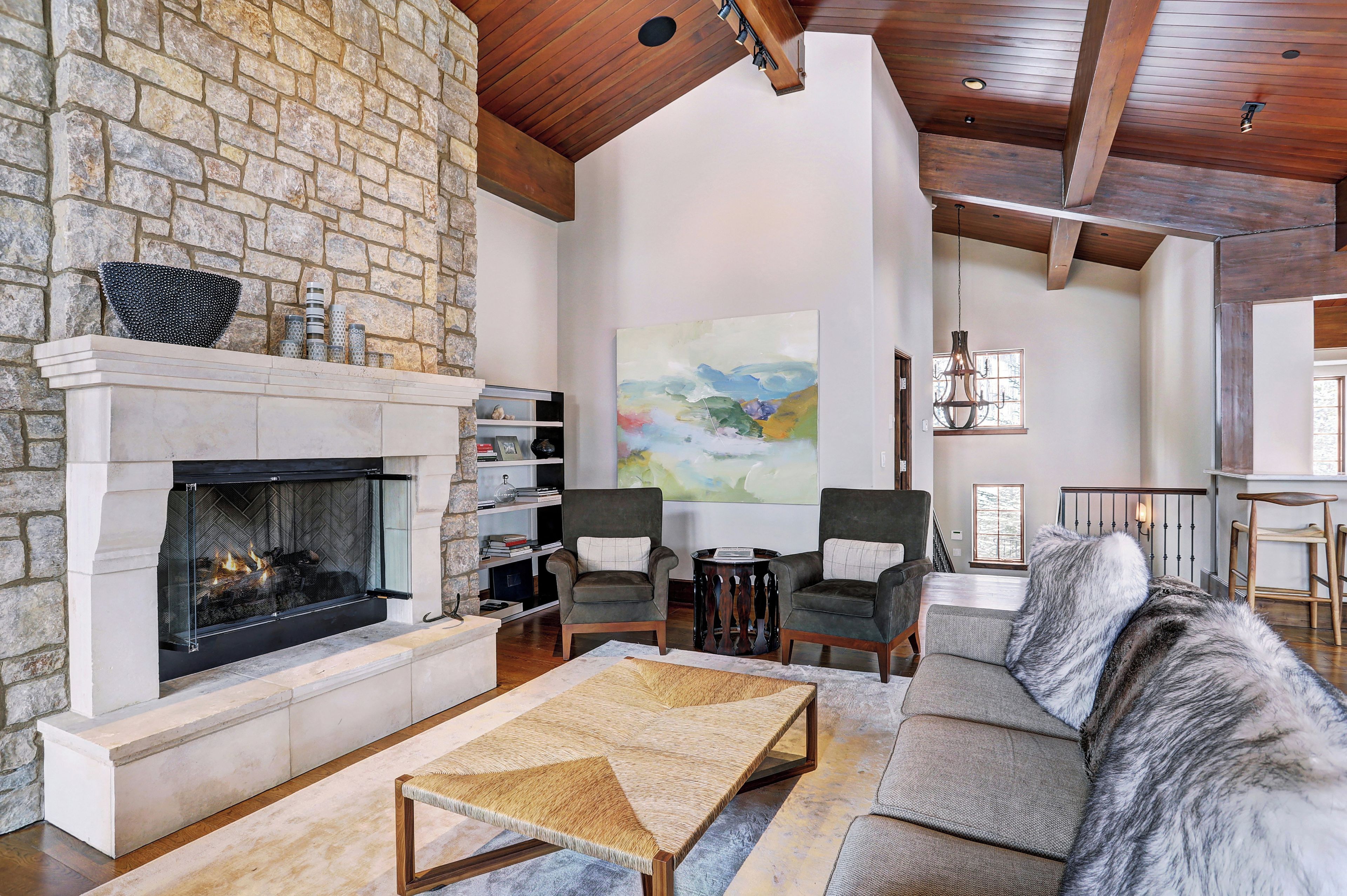 A spacious living room with a stone fireplace, comfortable seating, and a large painting on the wall.