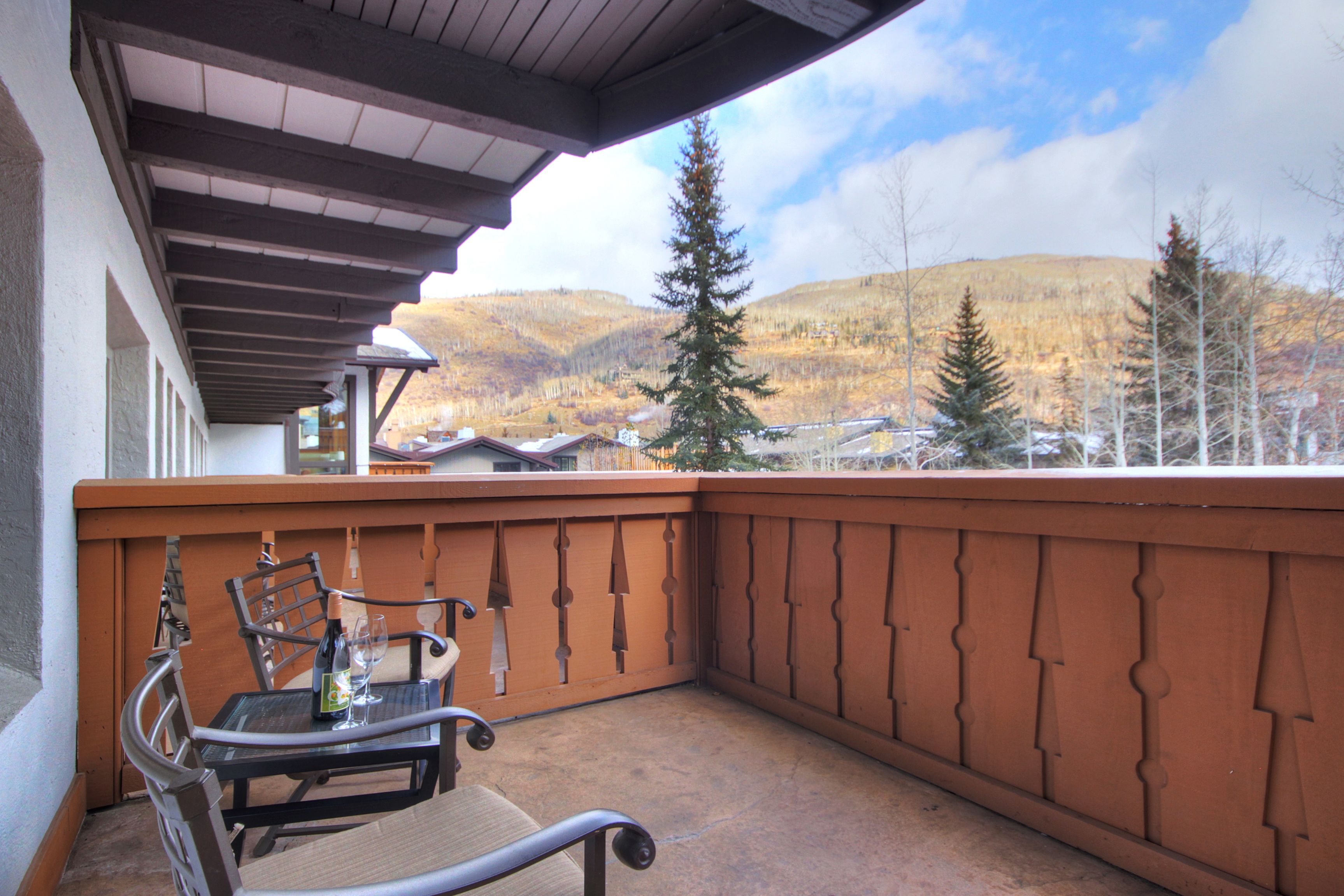 A balcony with a table and chairs, overlooking a mountainous landscape.
