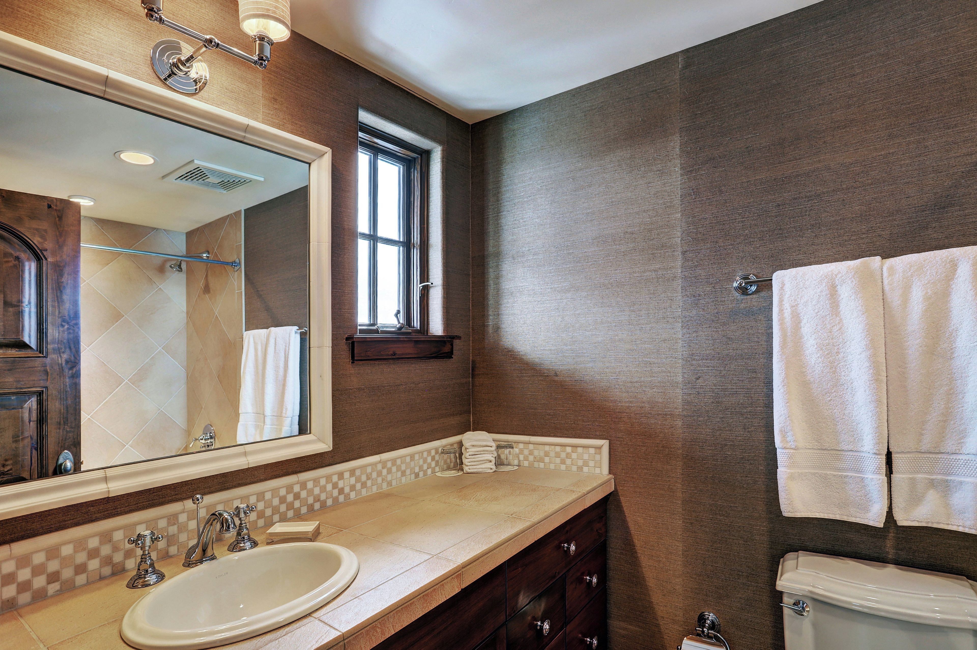 A bathroom with a large mirror, a sink, a toilet, and a window.