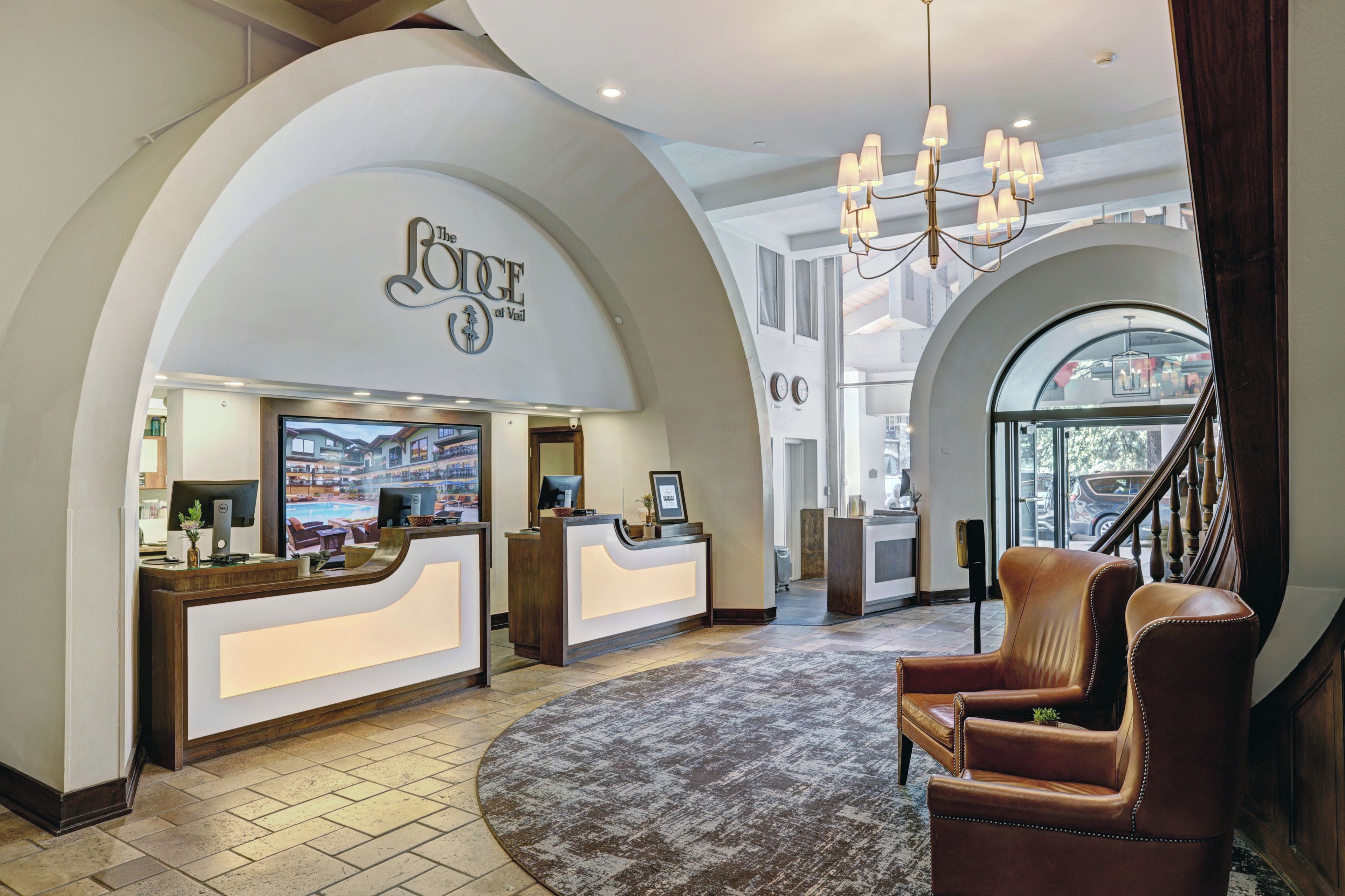 A hotel reception area with a reception desk, a chandelier, a leather armchair, and a large arched window.