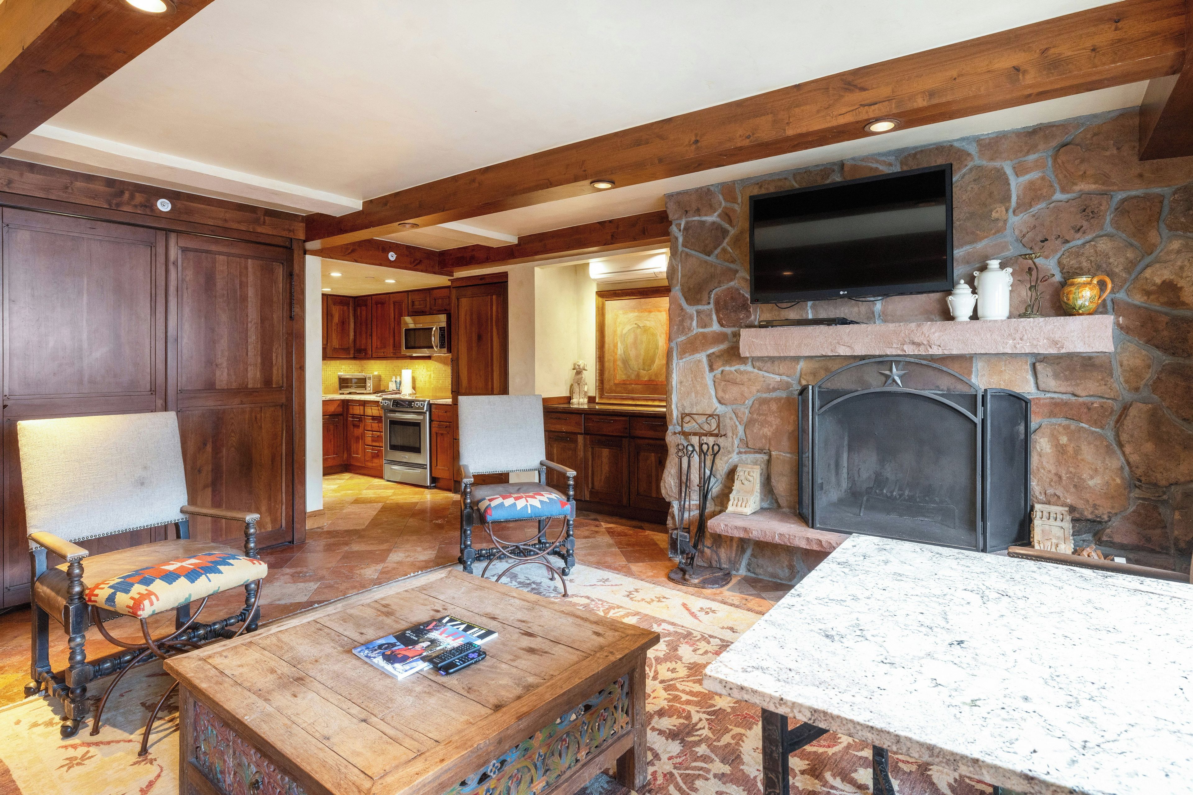 Una sala de estar acogedora con chimenea de piedra, muebles de madera y un televisor montado en la pared.