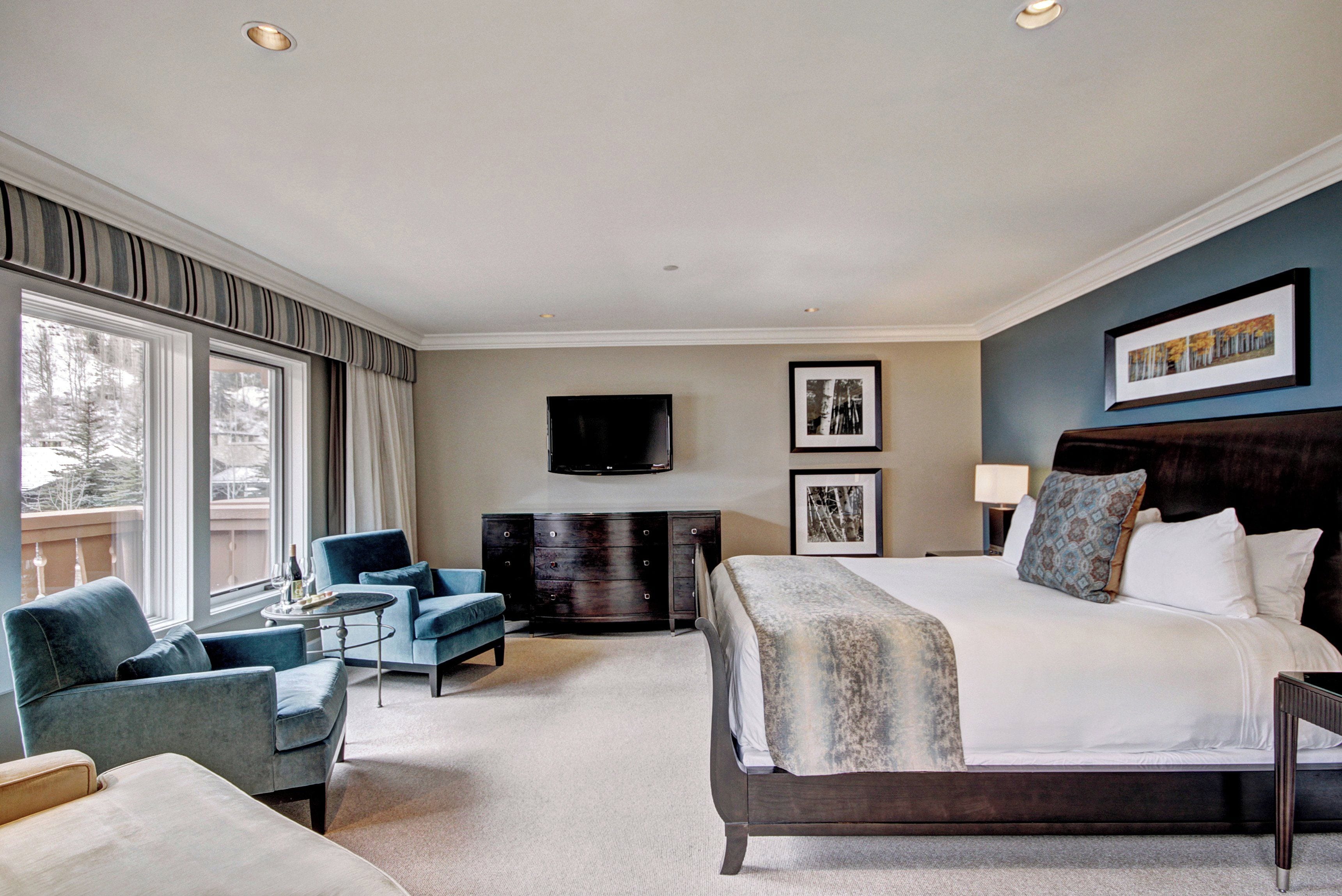 A hotel room with a large bed, a flat-screen TV mounted on the wall, a desk with a chair, and a window with curtains.