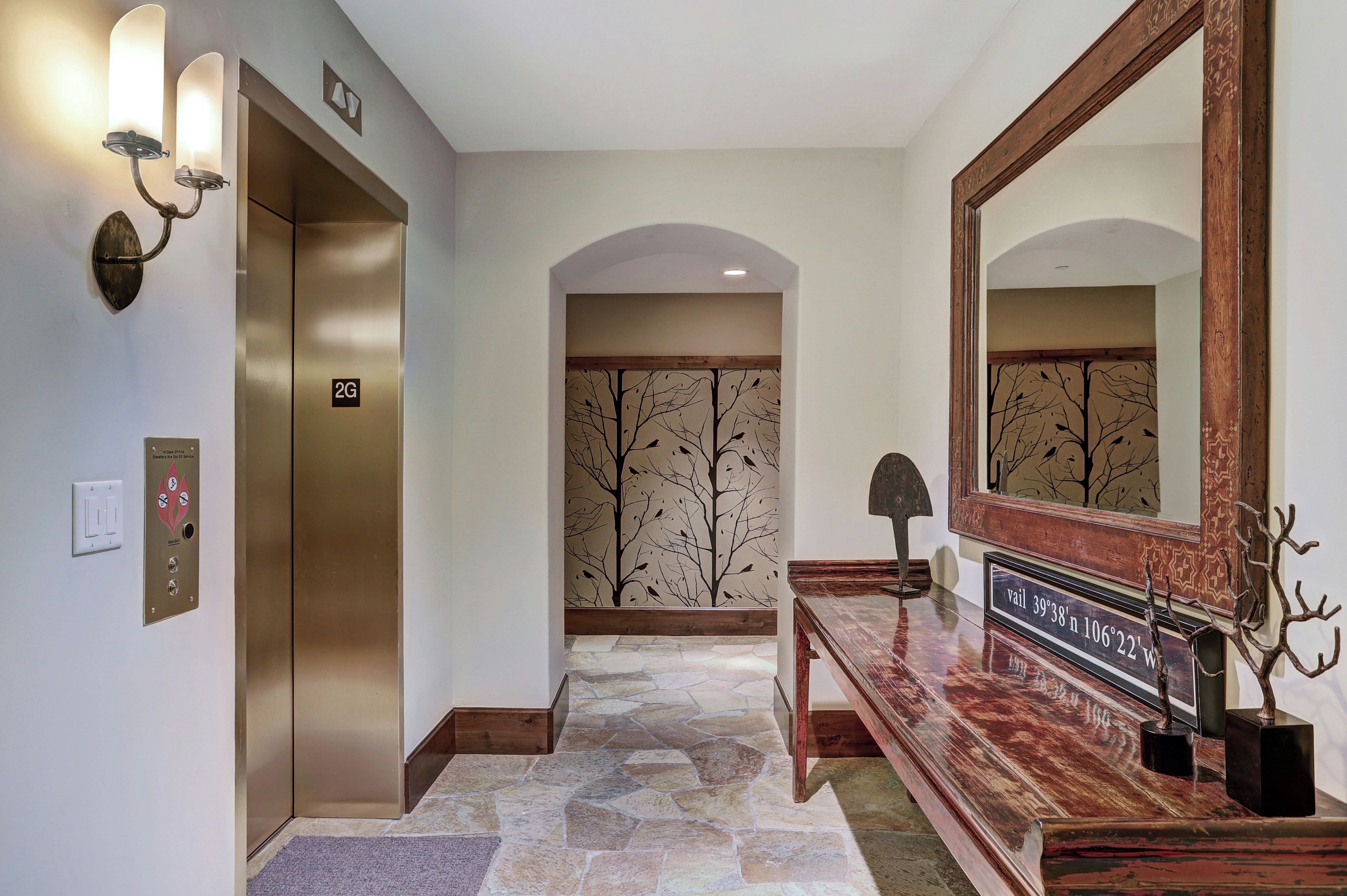 An elevator, a reception desk with a mirror, and a stone-tiled floor.