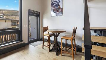 Una habitación con piso de madera, una mesa redonda con sillas, una puerta con la leyenda 'BORN FREE' y una ventana que ofrece vistas a una montaña.