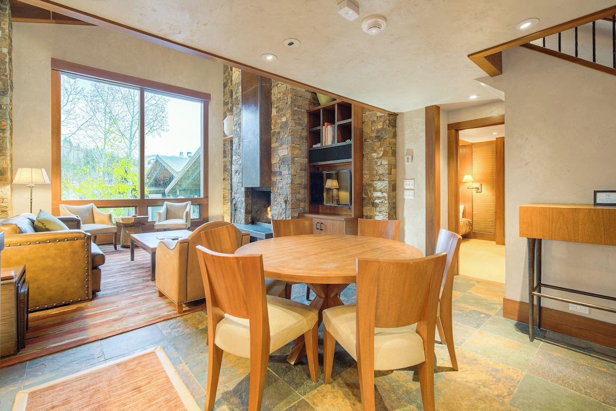 A spacious living area with a large round wooden table surrounded by chairs, a stone fireplace, and a cozy seating area with sofas and a coffee table.