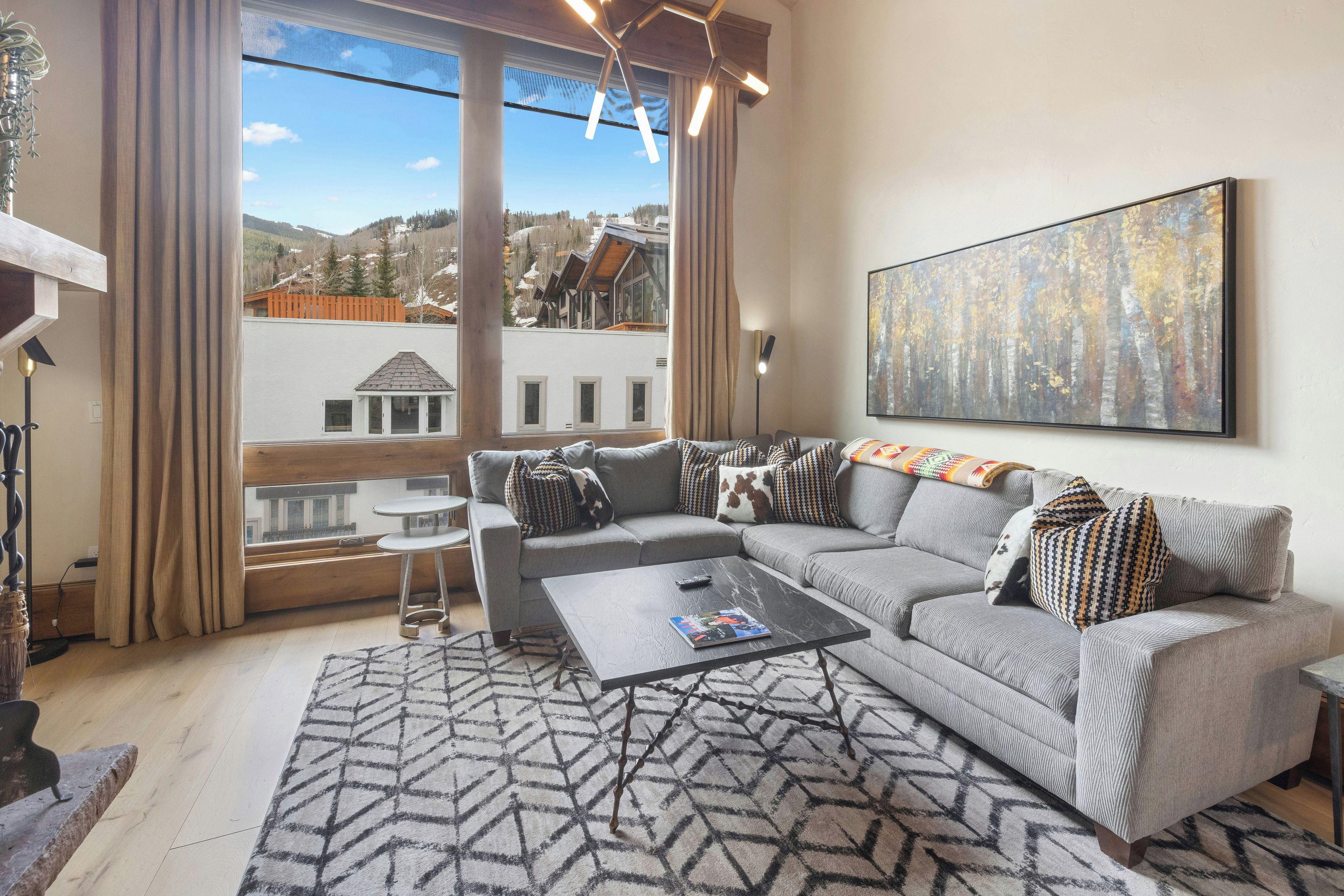 A modern living room with a large window, a gray sofa, a coffee table, and a patterned rug.