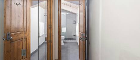A hallway leading to a bathroom with a shower, toilet, and a towel rack.