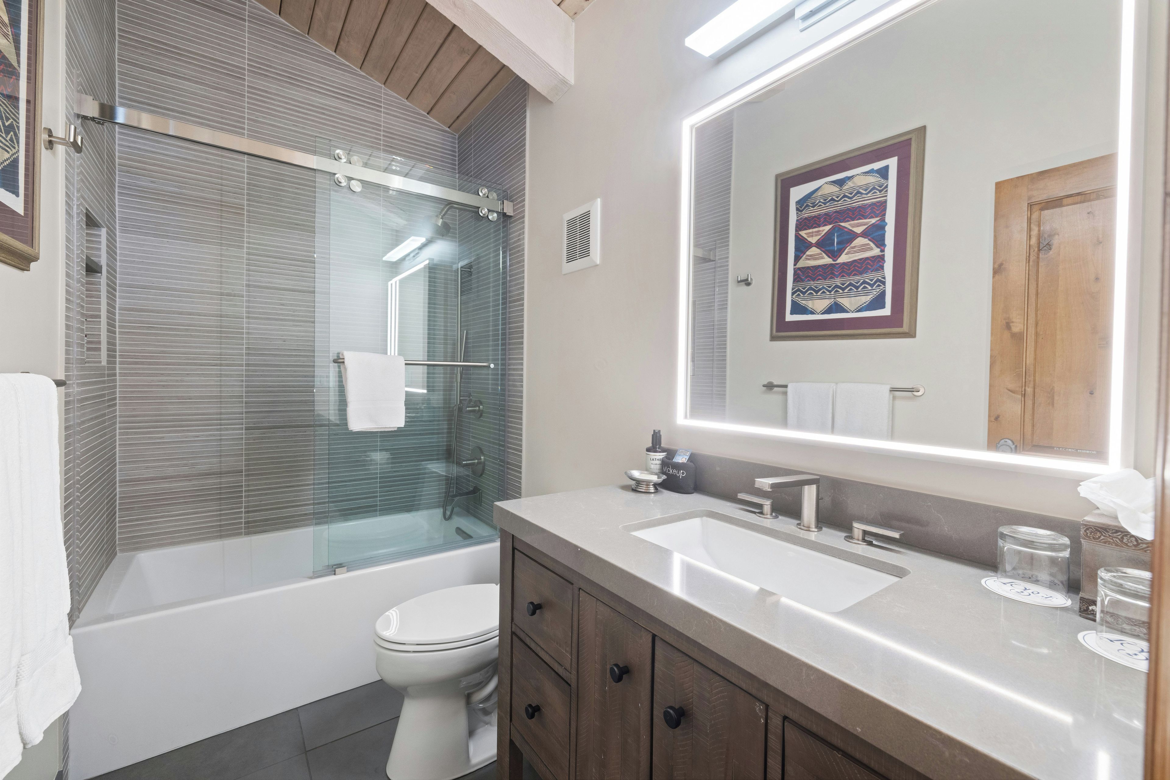 A modern bathroom with a glass-enclosed shower, a white toilet, a vanity with a sink, and a large mirror.